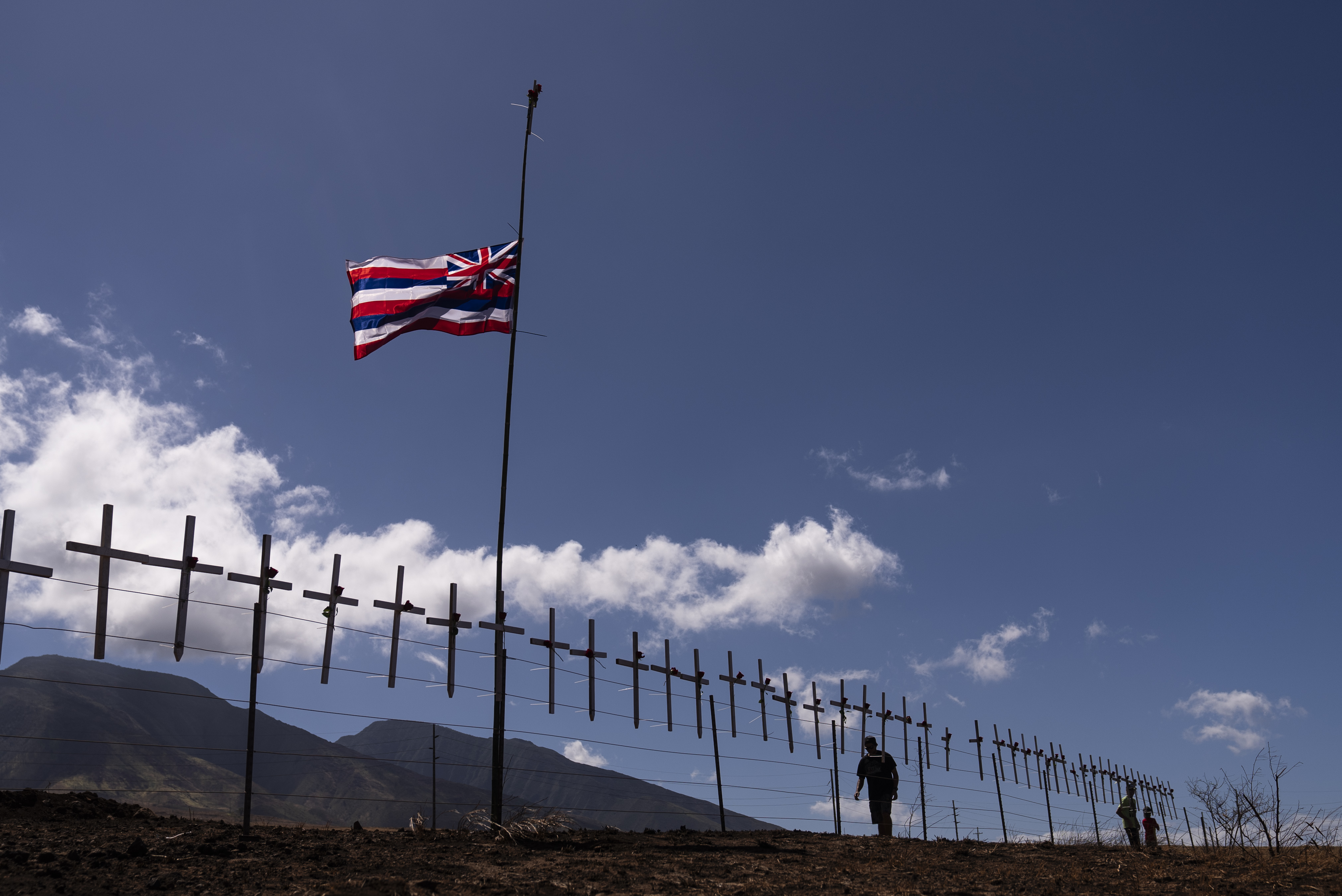 Crosses honoring the victims killed in a recent wildfire hang on a fence along the Lahaina Bypass as a Hawaiian flag flutters in the wind in Lahaina, Hawaii, Tuesday. Authorities say anywhere between 500 and 1,000 people remain unaccounted for. 