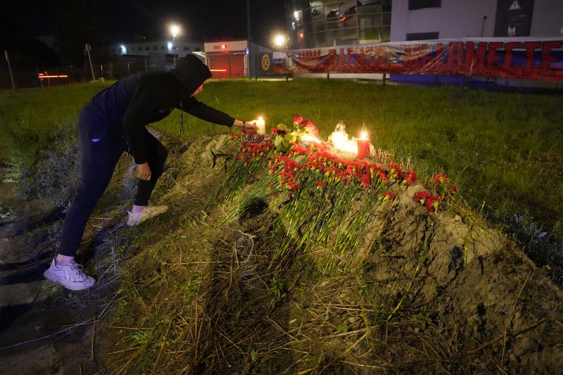 A man lights a candle at an informal memorial next to the former 'PMC Wagner Centre' in St. Petersburg, Russia, Thursday with a banner with words reading 'PMC Wagner, we are together' in the background.