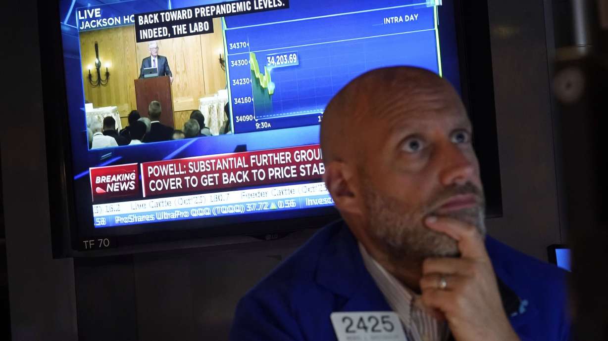 Specialist Meric Greenbaum works at his post on the floor of the New York Stock Exchange on Friday as Federal Reserve Chair Jerome Powell’s speech shows on a television screen. Stocks are holding on to gains after Powell said more rate hikes could be on the way to continue the Fed’s fight against inflation.