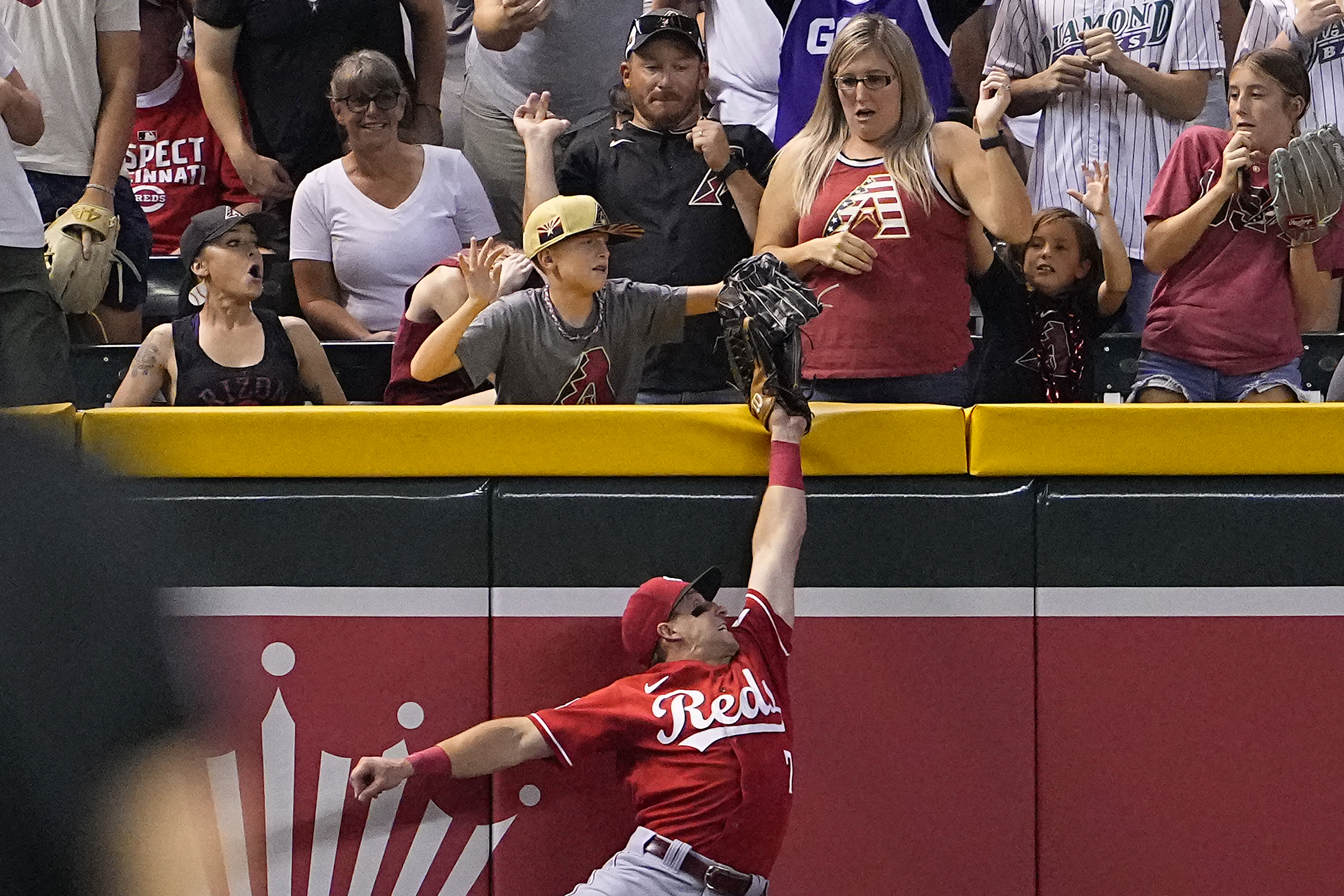 CORRECTS THAT FAN WAS MOVED, NOT EJECTED - A young fan pulls the ball out of the glove of Cincinnati Reds' Spencer Steer on a ball hit by Arizona Diamondbacks' Tommy Pham during the seventh inning of a baseball game, Friday, Aug. 25, 2023, in Phoenix. The fan was called for interference on the play, and was moved to a different seating area.