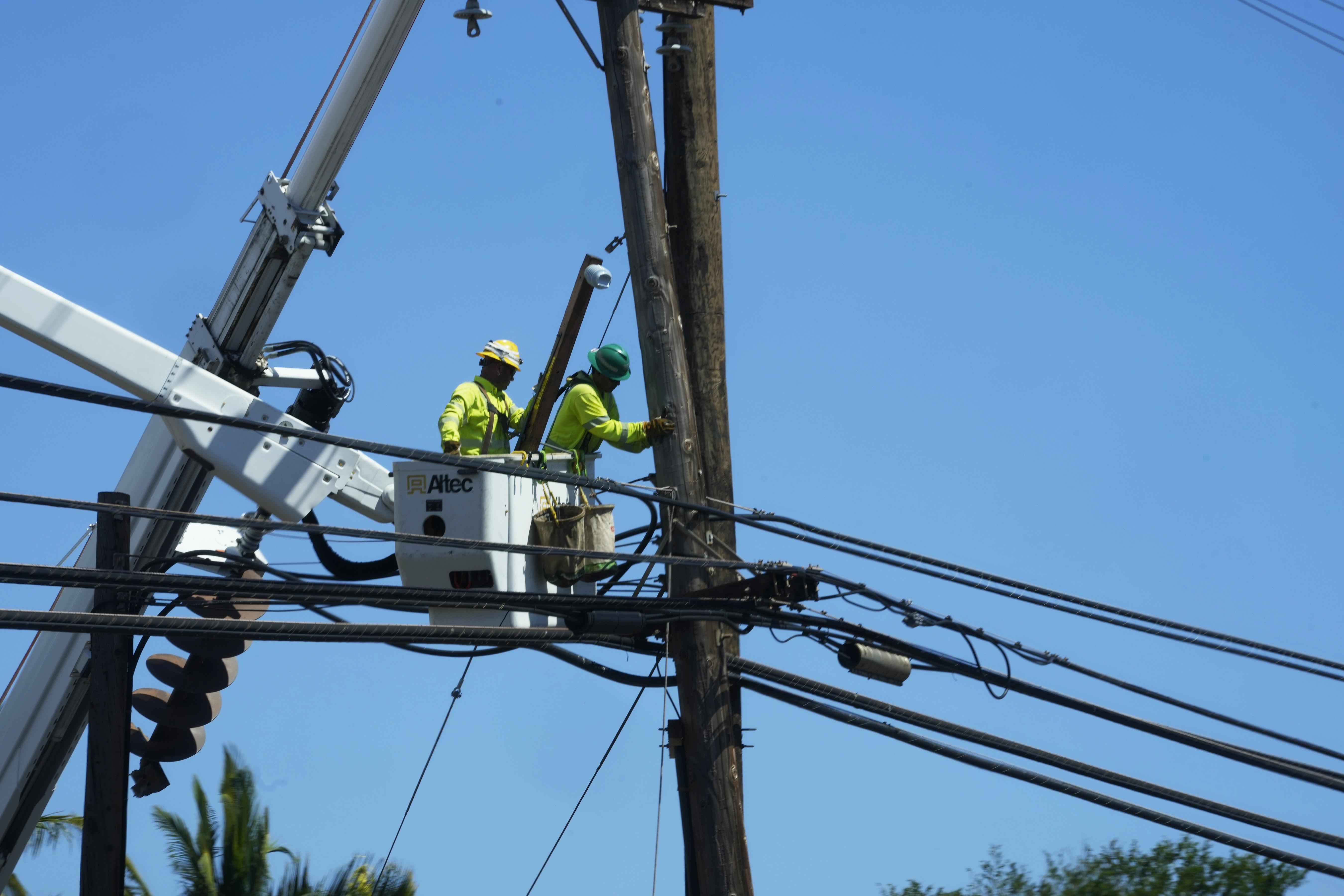 Linemen work on poles Aug. 13, in Lahaina, Hawaii, following a deadly wildfire that caused heavy damage days earlier. When the winds of Hurricane Dora lashed Maui Aug. 8, they struck bare electrical lines the Hawaiian electric utility had left exposed to the elements.