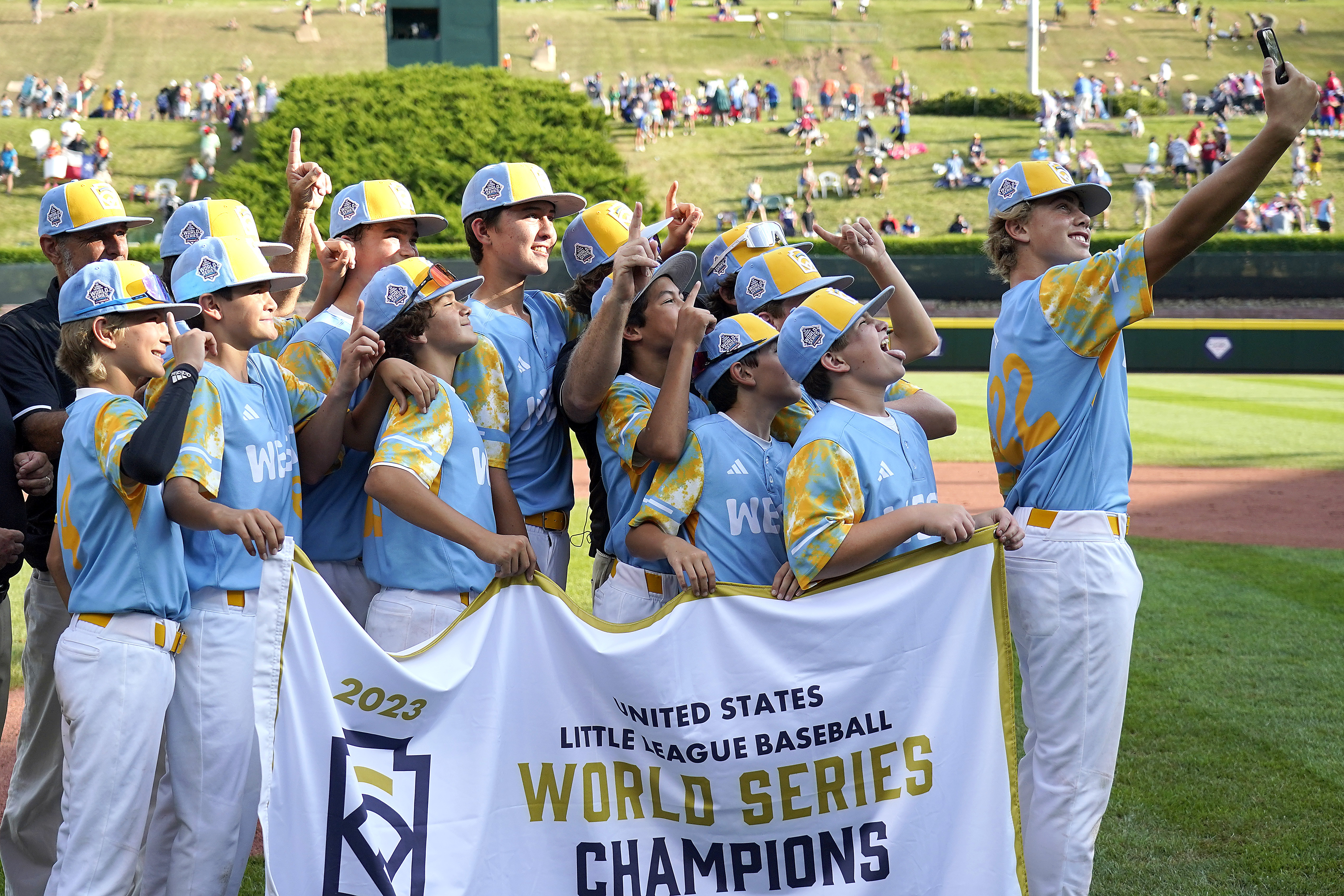 El Segundo, Calif.'s Jaxon Kalish (22) takes a photo with the team and the championship banner after they defeated Needville, Texas, in the United States Championship baseball game at the Little League World Series tournament in South Williamsport, Pa., Saturday, Aug. 26, 2023. 