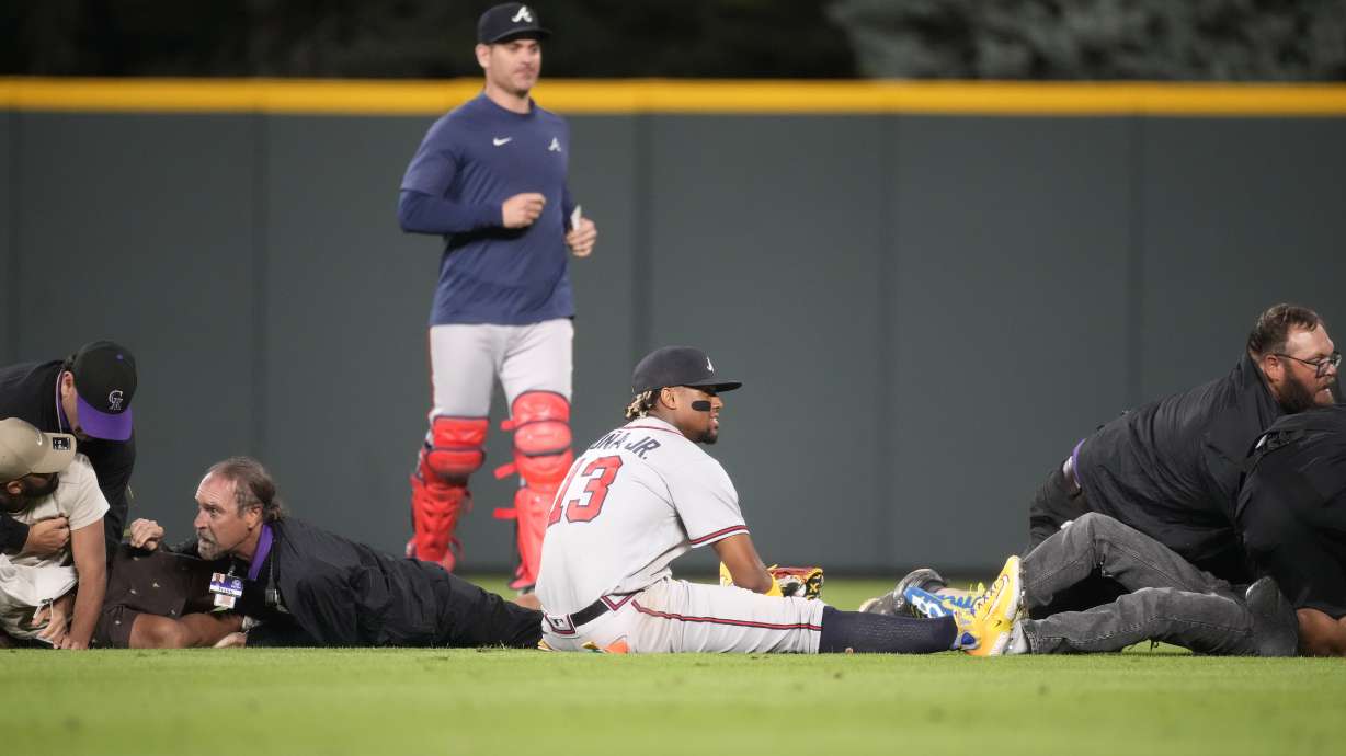 Atlanta Braves right fielder Ronald Acuna Jr., bottom center, ends up on the turf as field guards wrestle down two fans who approached him as he took his spot in the field for the bottom of the seventh inning of a baseball game against the Colorado Rockies, Monday, Aug. 28, 2023, in Denver.