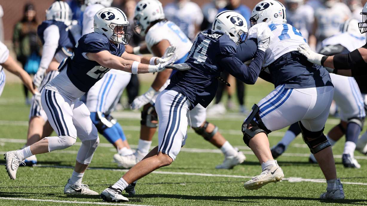 BYU safety Ethan Slade and linebacker Maika Kaufusi battle offensive lineman Trevin Ostler as the BYU Cougars football team practices in Provo on Friday, March 17, 2023.