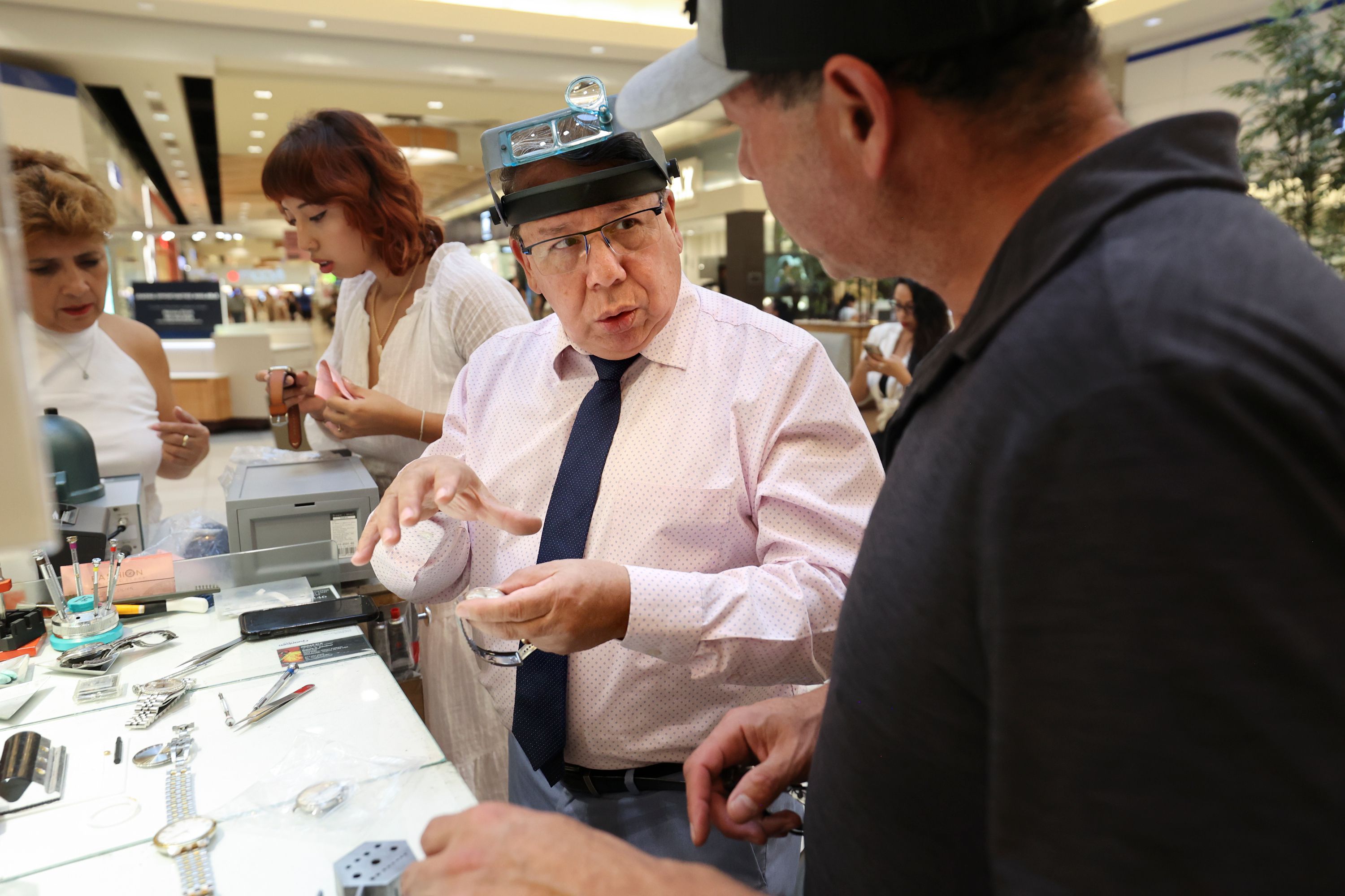 Marcelo Sandivar, certified watch technician and owner of Fashion Watch & Clock, helps a customer at the company’s kiosk in Fashion Place Mall in Murray on Aug. 24. His wife and granddaughter work behind him.