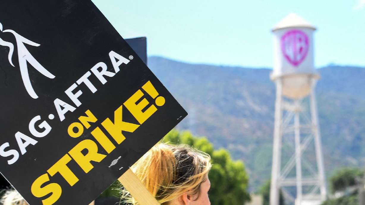 Members of the Writers Guild of America and the Screen Actors Guild walk a picket line outside of Warner Bros Studio in Burbank, Calif., on July 26. Warner Bros. Discovery trimmed its full-year earnings guidance for 2023 on Tuesday by $300 million to $500 million because of the continued strike.