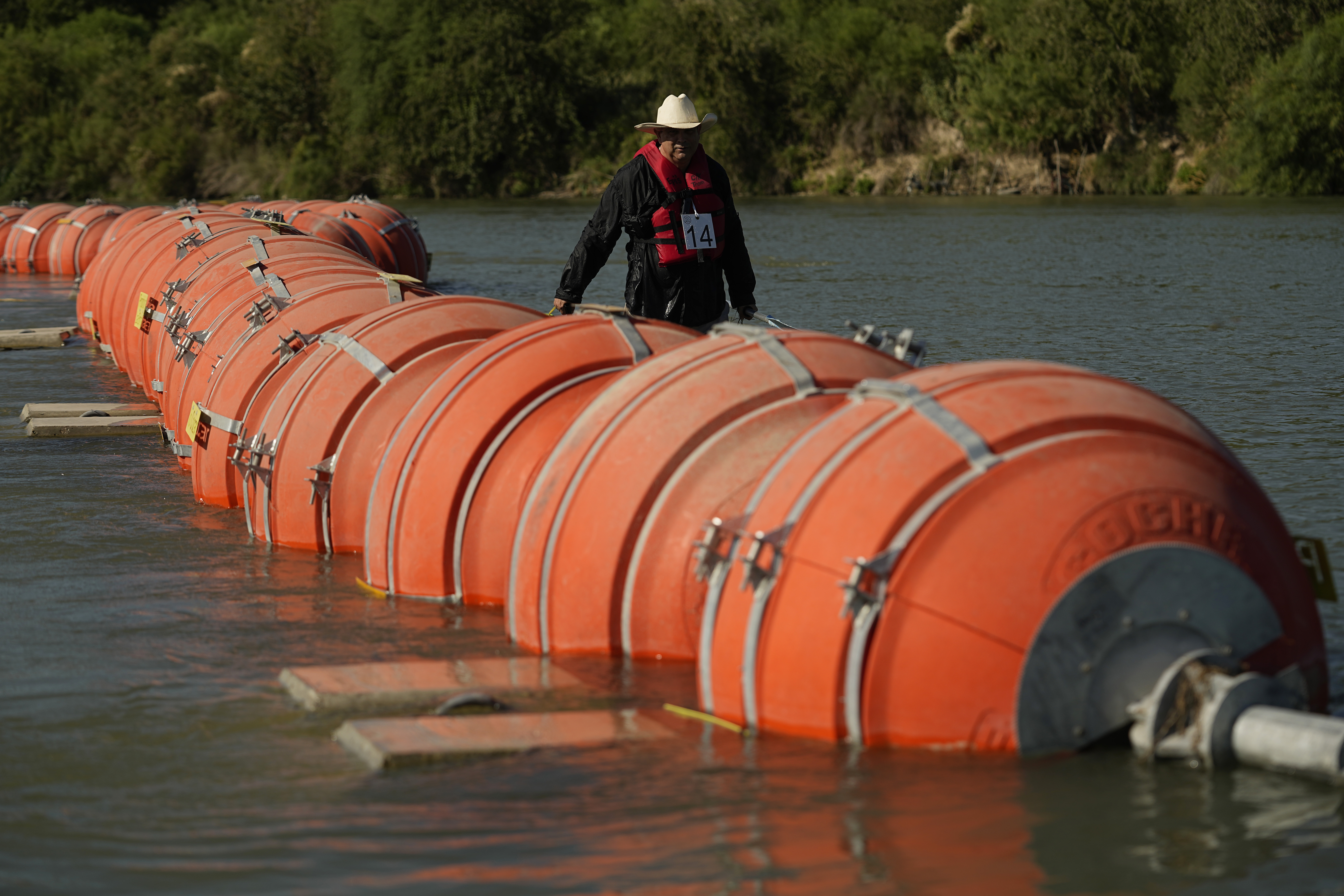 A kayaker walks past large buoys being used as a floating border barrier on the Rio Grande, Aug. 1, in Eagle Pass, Texas. A federal judge on Wednesday ordered Texas to move a large floating barrier to the riverbank of the Rio Grande after protests from the U.S. and Mexican governments over Republican Gov. Greg Abbott’s latest tactic to stop migrants from crossing America’s southern border.