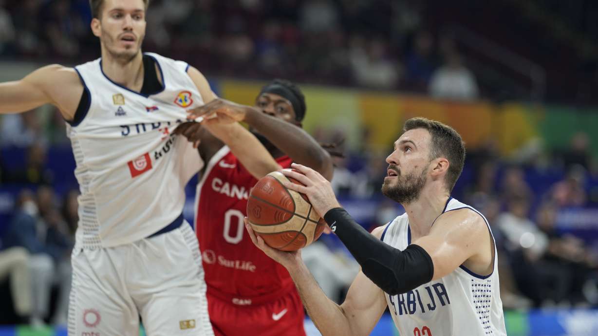 Serbia guard Marko Guduric, right, prepares to shoot as Canada guard Luguentz Dort, center, is held back during a Basketball World Cup semi final game in Manila, Philippines, Friday, Sept. 8, 2023.