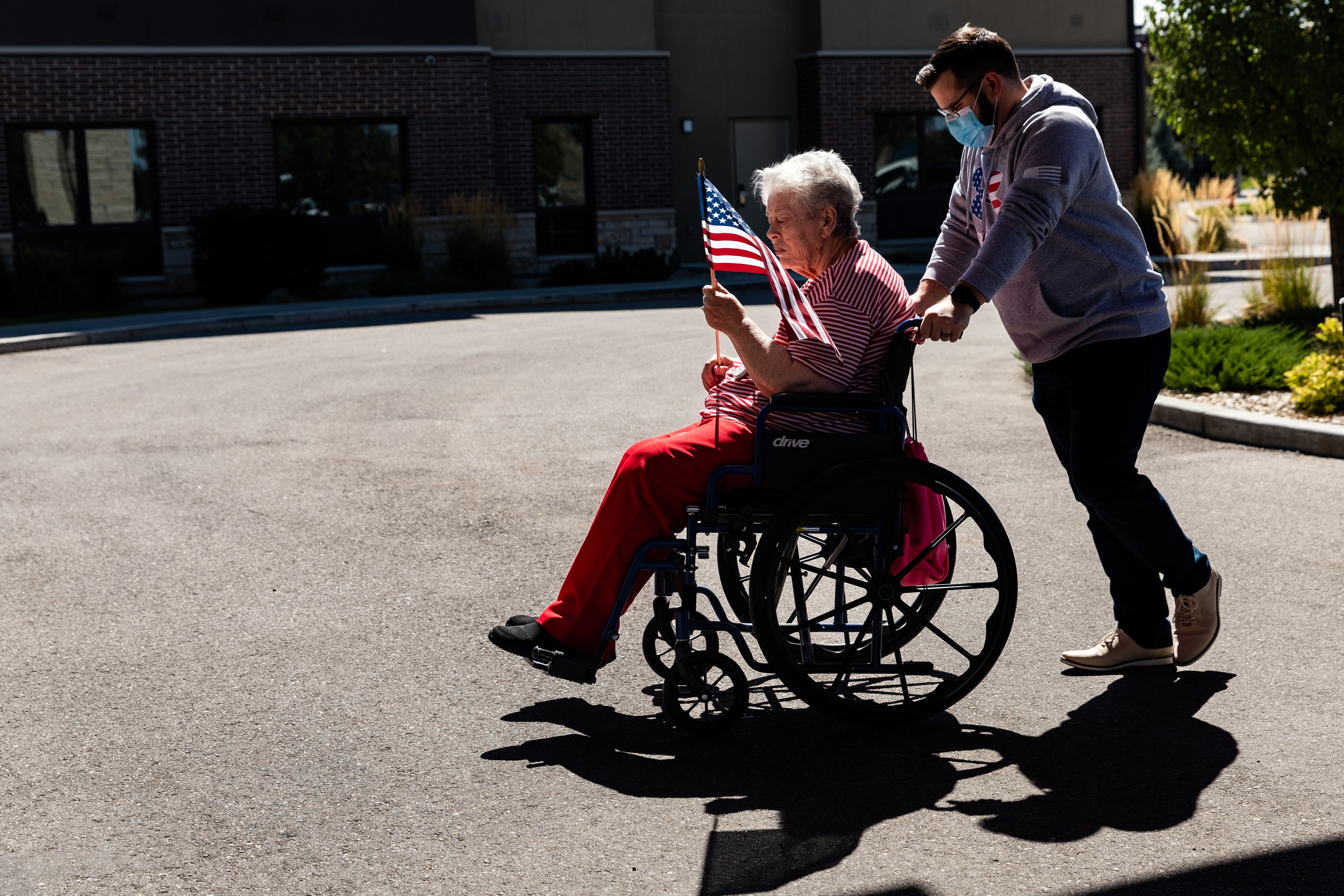 Gabryel Souto Correia helps take Joan Christensen to place a flag at a 9/11 memorial tribute at Copper Creek Senior Living in South Jordan on Monday. Every resident was invited to put up a flag and share with caretakers where they were on 9/11.