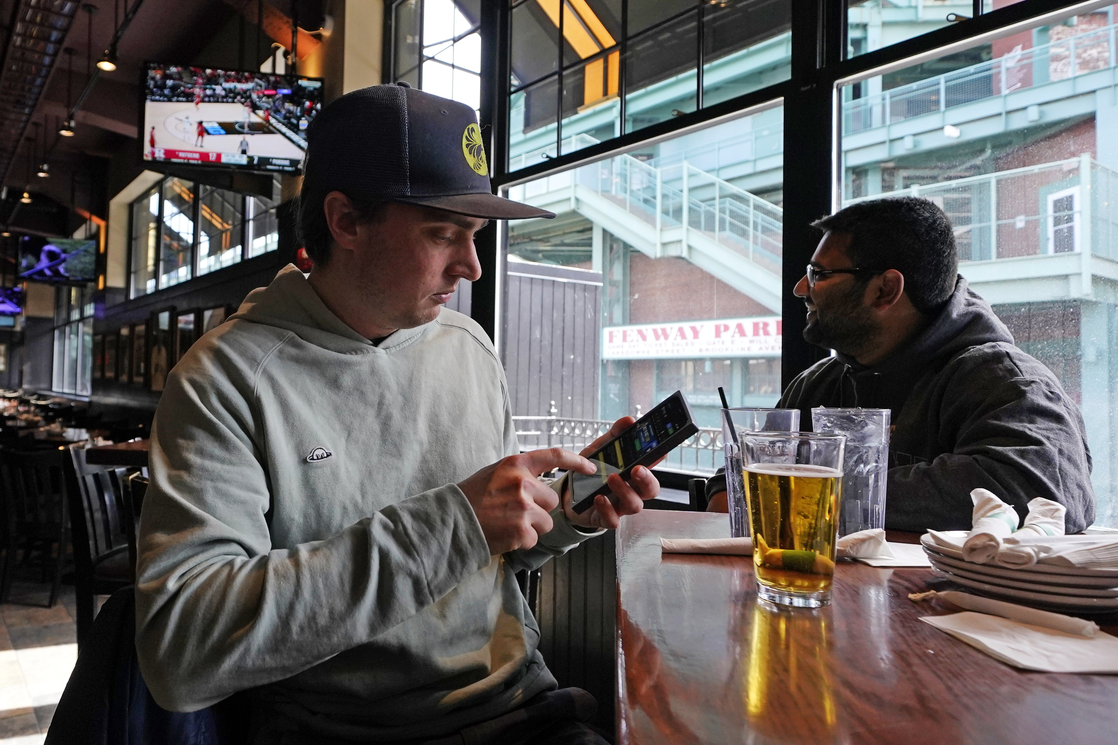 FILE - Taylor Foehl, left, of Boston, looks at the mobile betting app on his phone after placing a wager, while watching a men's college basketball game at the Cask 'N Flagon sports bar, Friday, March 10, 2023, near Fenway Park in Boston. A company that most of the legal U.S. sports betting industry uses to verify that its customers are where they say they are reported on Wednesday, Sept. 13, a record number of transactions over the first weekend of the NFL season.