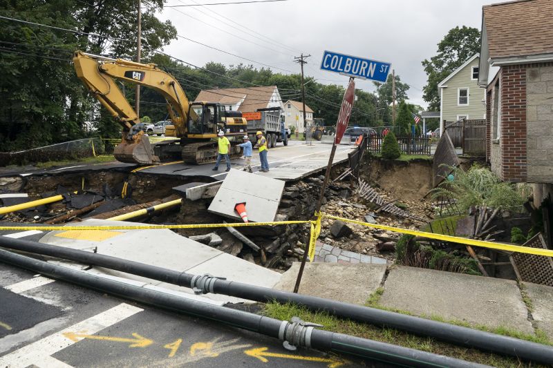 Public works officials examine the damage to a road and front yard that was washed away by recent flooding, Wednesday in Leominster, Mass.
