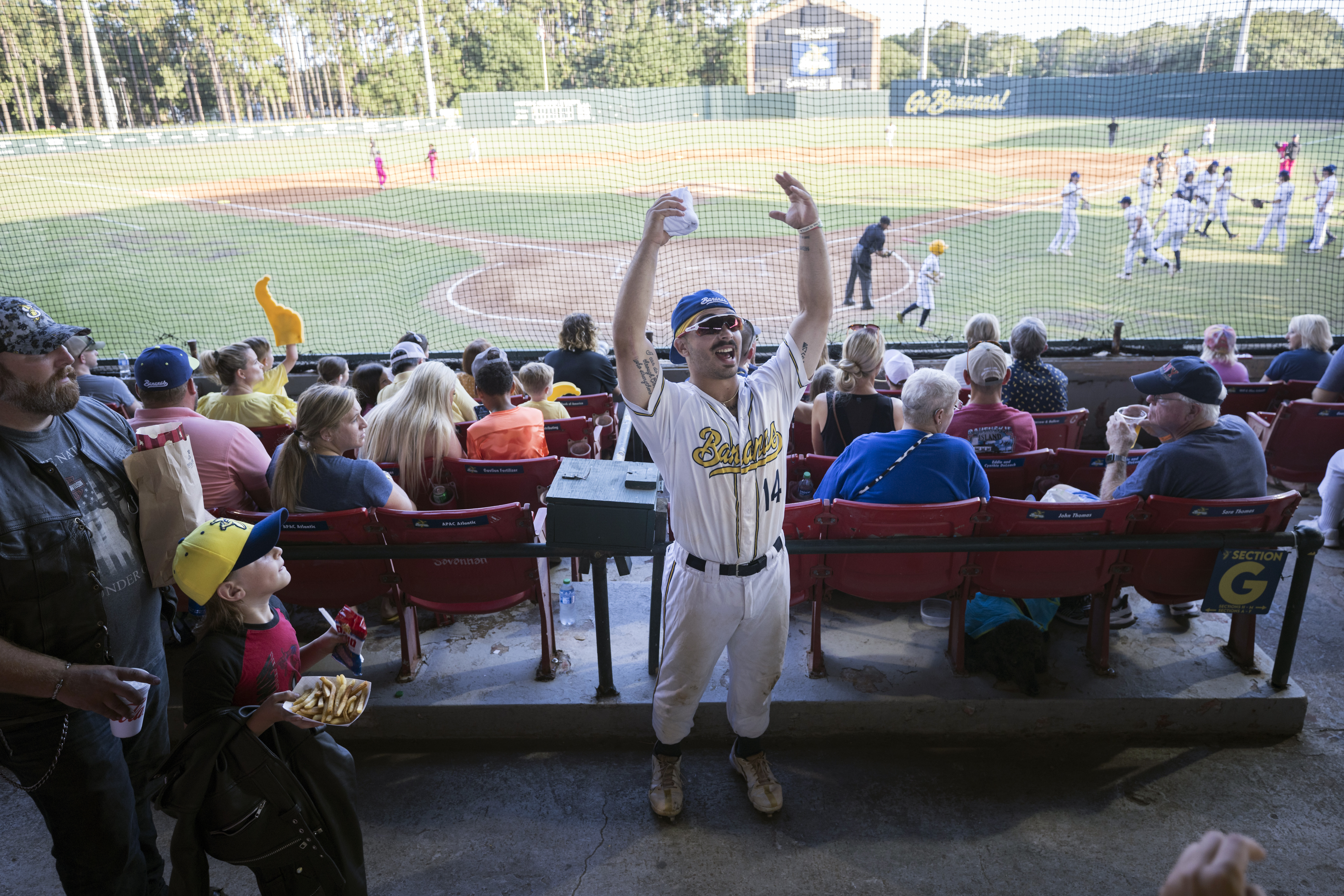 Savannah Bananas catcher Vinny Rauso, center, tries to get fans to cheer before throwing a free T-shirt to the loudest section, during the team's baseball game against the Florence Flamingos, June 7, 2022, in Savannah, Ga.