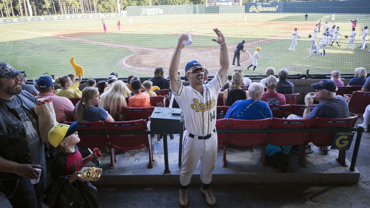 FILE - Savannah Bananas catcher Vinny Rauso, center, tries to get fans to cheer before throwing a free T-shirt to the loudest section, during the team's baseball game against the Florence Flamingos, June 7, 2022, in Savannah, Ga. A new exhibit dedicated to the sport's wackiest team, the Bananas, will open Friday at the Baseball Hall of Fame in Cooperstown, N.Y.