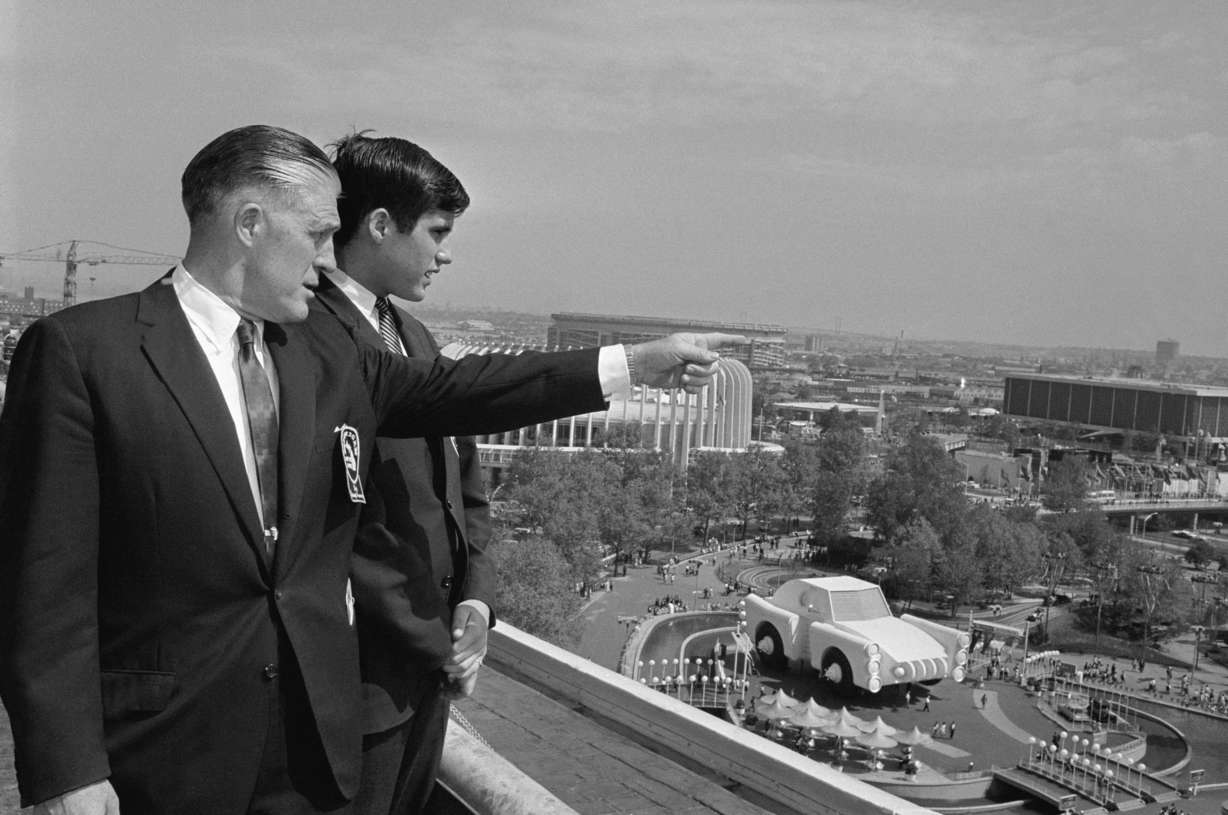 In this May 18, 1964, file photo Gov. George Romney and his son, Mitt, look out over the New York World's Fair grounds from the heliport after attending a Michigan breakfast at the Top of the Fair Restaurant. The governor and a large delegation from Michigan were there for Michigan Day at the fair. At right is part of the Chrysler exhibit and behind them is the Ford exhibit.