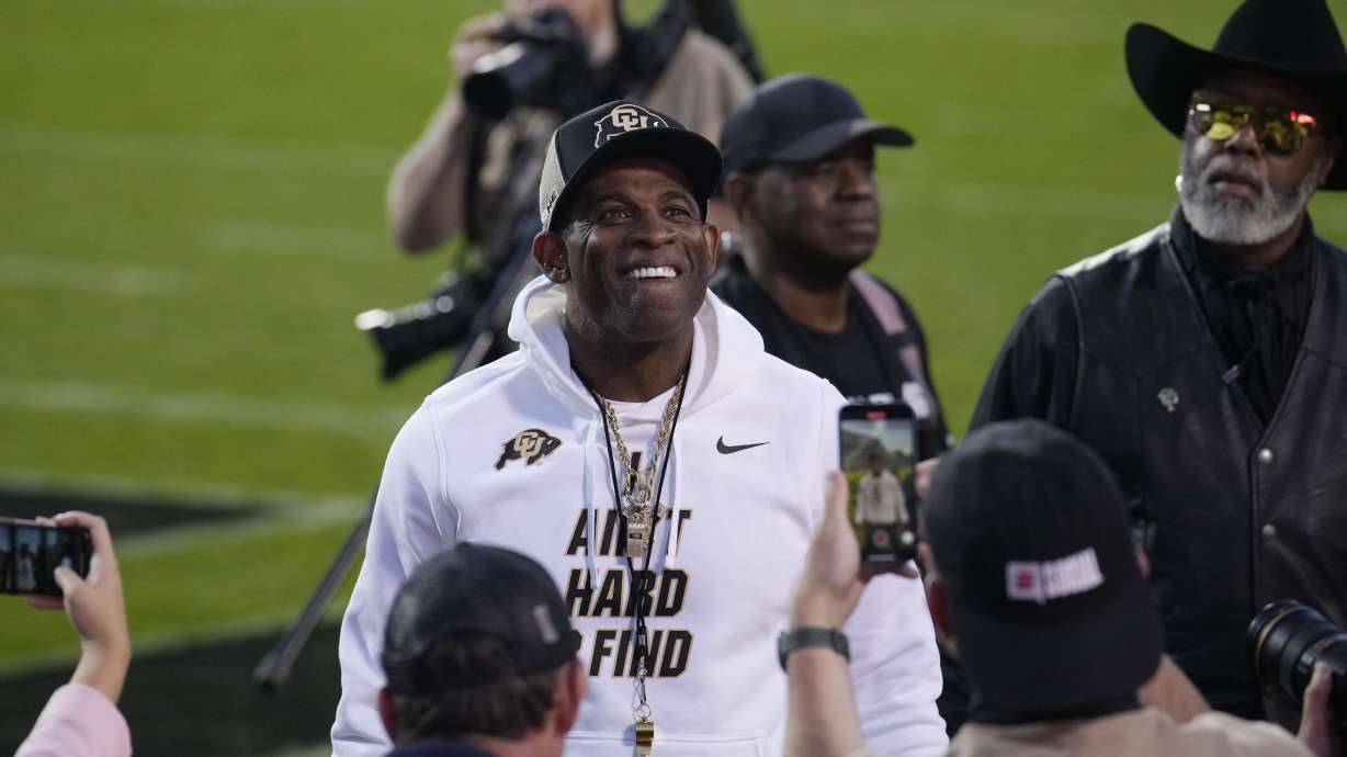 Colorado head coach Deion Sanders, center, stops and pulls off his sunglasses and smiles for the crowd as players warm up before an NCAA college football game against Colorado State, Saturday, Sept. 16, 2023, in Boulder, Colo.