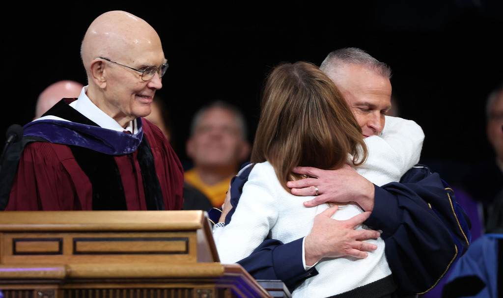 BYU President C. Shane Reese hugs his wife Wendy Reese at his installation as BYU’s 14th president at the Marriott Center in Provo on Tuesday. President Dallin H. Oaks, first counselor in the First Presidency of The Church of Jesus Christ of Latter-day Saints, looks on.