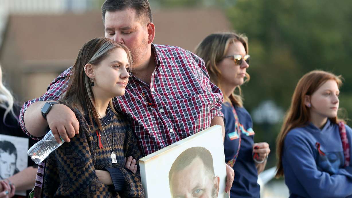 Matt Gwyther kisses his daughter Jo Gwyther while holding a photo of his late husband Dennis Gwyther at Utah's National Day of Remembrance for Homicide Victims event outside of the Capitol in Salt Lake City on Monday.