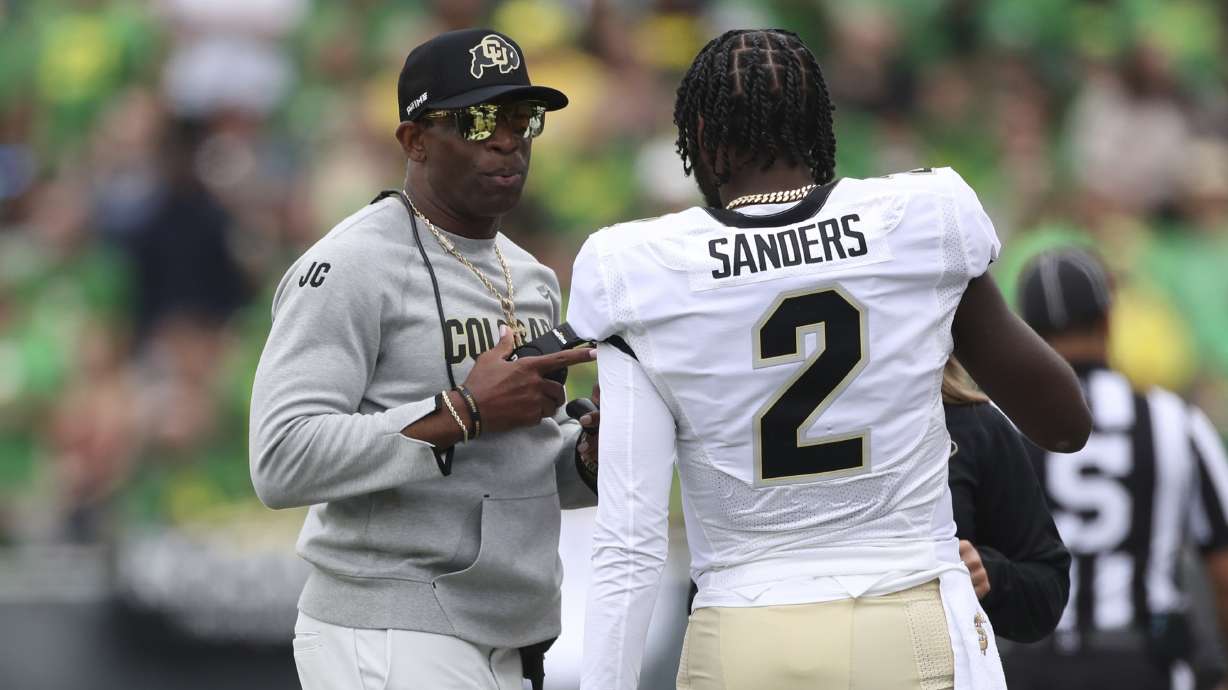 Colorado head coach Deion Sanders talks with his son and quarterback Shedeur Sanders during the first half of an NCAA college football game against Oregon, Saturday, Sept. 23, 2023, in Eugene, Ore.
