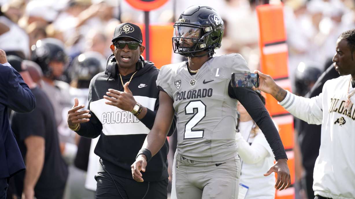 Colorado head coach Deion Sanders, left, talks with his son, quarterback Shedeur Sanders, before the first half of an NCAA college football game against Southern California Saturday, Sept. 30, 2023, in Boulder, Colo.