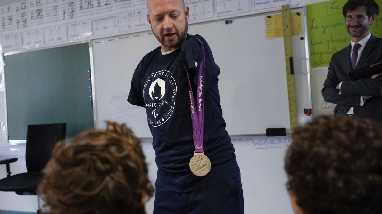 Archer Matt Stutzman of United States shows his silver medal from the Paralympic Games in 2012 to pupils, in a Paris school, in Paris, Wednesday, Oct. 4, 2023. Visiting France's capital before Paralympic tickets go on sale next week, Stutzman dropped by a Paris school on Wednesday and wowed its young pupils with his shooting skills.