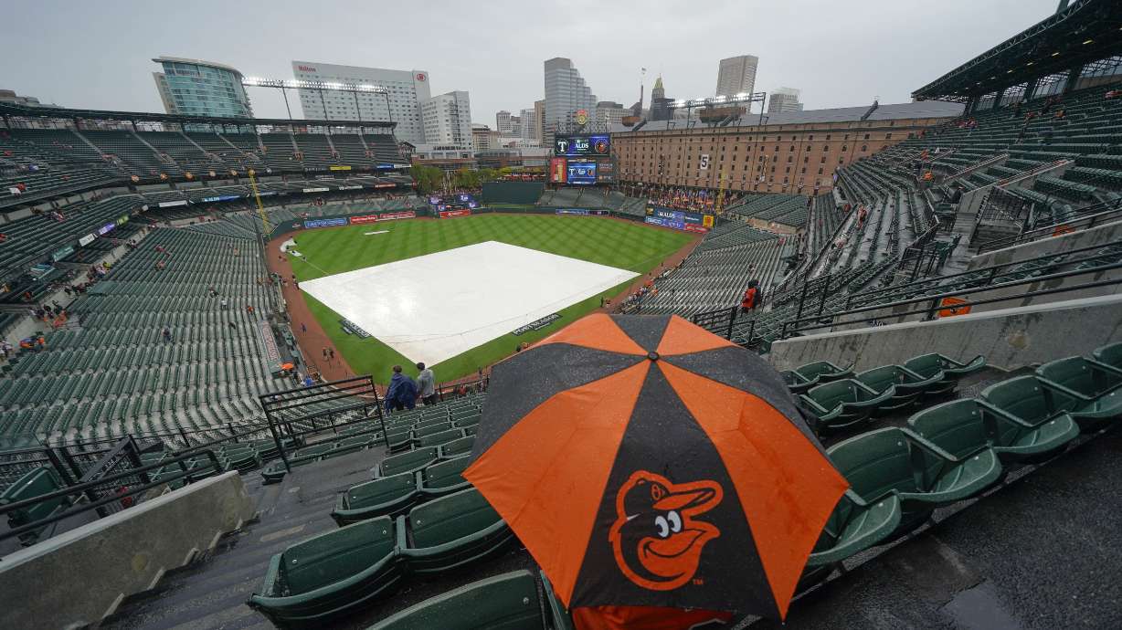A fan sits in the stand with an umbrella as they wait for the start of Game 1 of an American League Division Series baseball game between the Baltimore Orioles and the Texas Rangers, Saturday, Oct. 7, 2023, in Baltimore, Md.