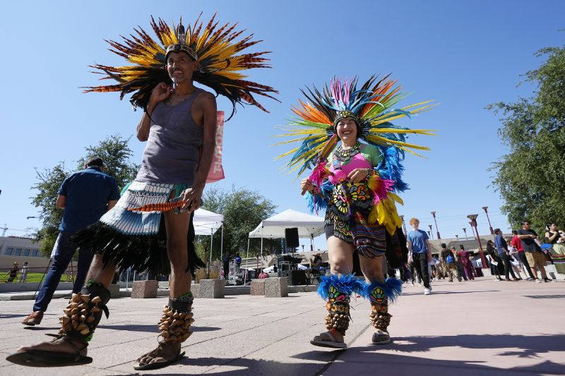 People wearing traditional Aztec dance clothing walk through an Indigenous Peoples Day festival, Monday in Phoenix.