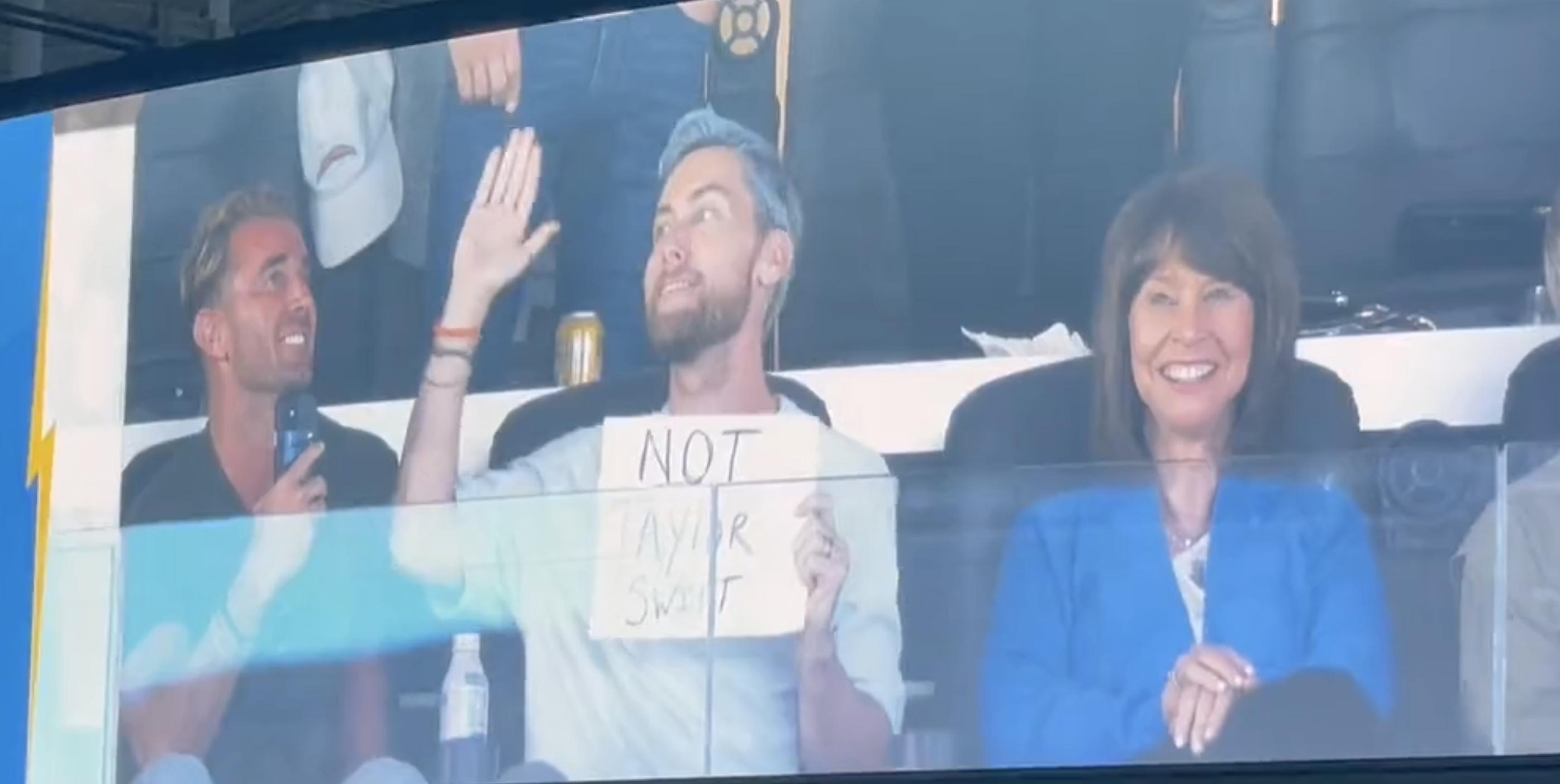 NSYNC's Lance Bass holds up a sign reading "Not Taylor Swift" from his private suite during the Los Angeles Chargers' game against the Dallas Cowboys, Monday, Oct. 16, 2023 in Inglewood, California.