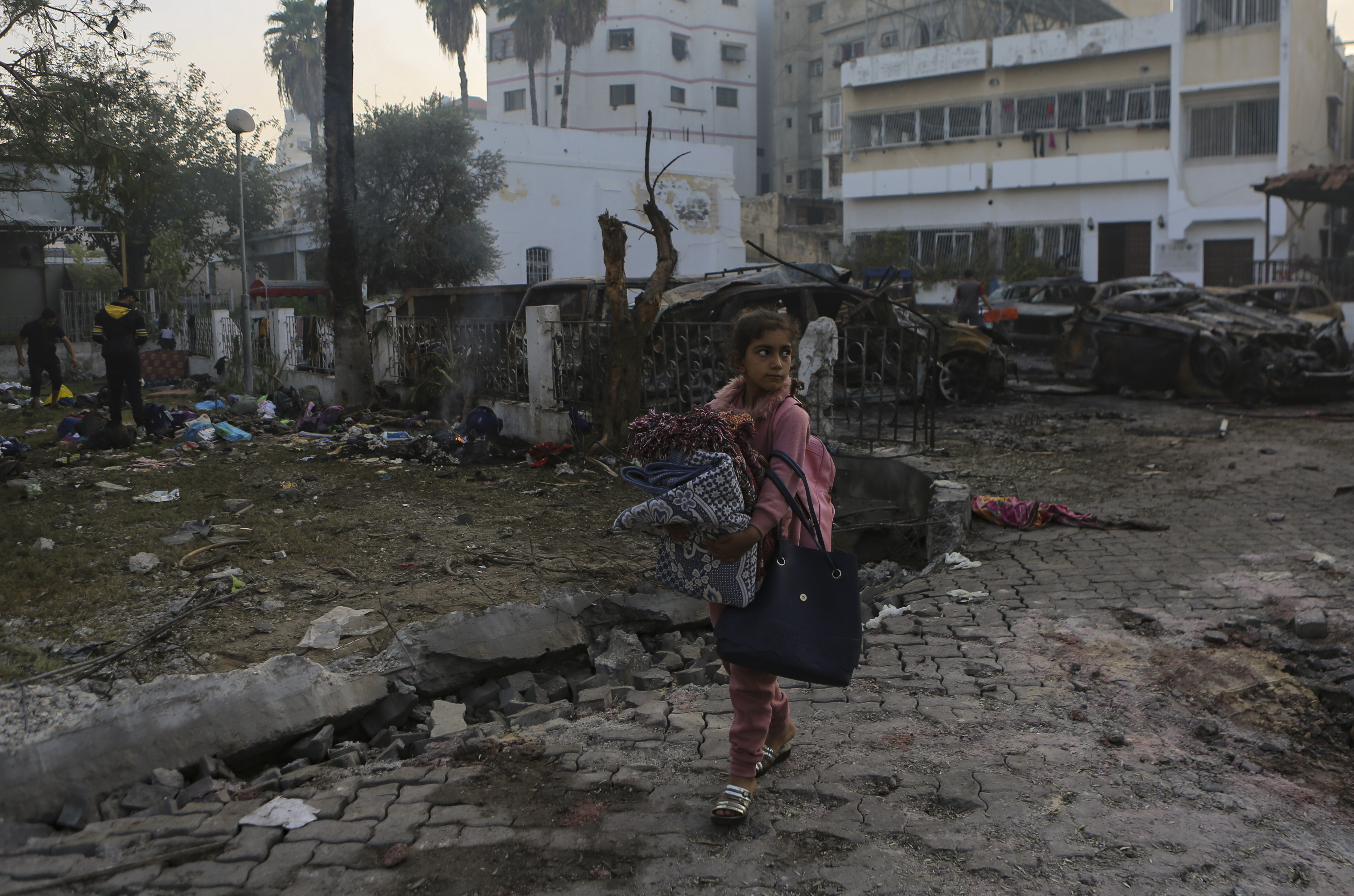 A Palestinian girl carries blankets as she walks past the site of a deadly explosion at al-Ahli hospital, in Gaza City, Oct. 18. Hamas says an Israeli airstrike caused the explosion, but the Israeli military says it was a misfired Palestinian rocket.