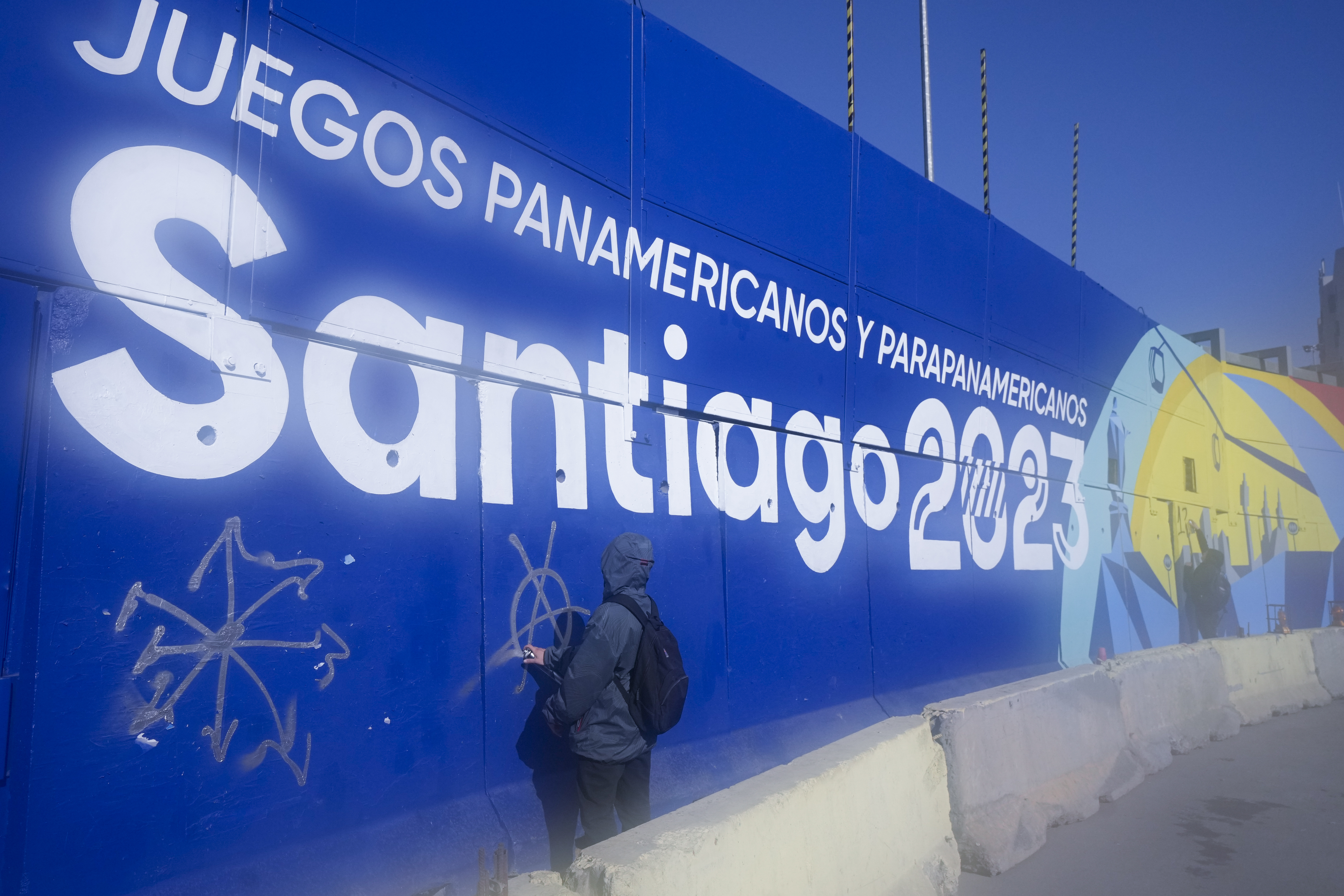 A demonstrator paints graffiti on a billboard advertising the Santiago 2023 Pan American Games, during protests marking the fourth anniversary of anti-government protests, in Santiago, Chile, Wednesday, Oct. 18, 2023. The opening ceremony for the XIX Pan American Games will take place in Santiago on Oct. 20. 