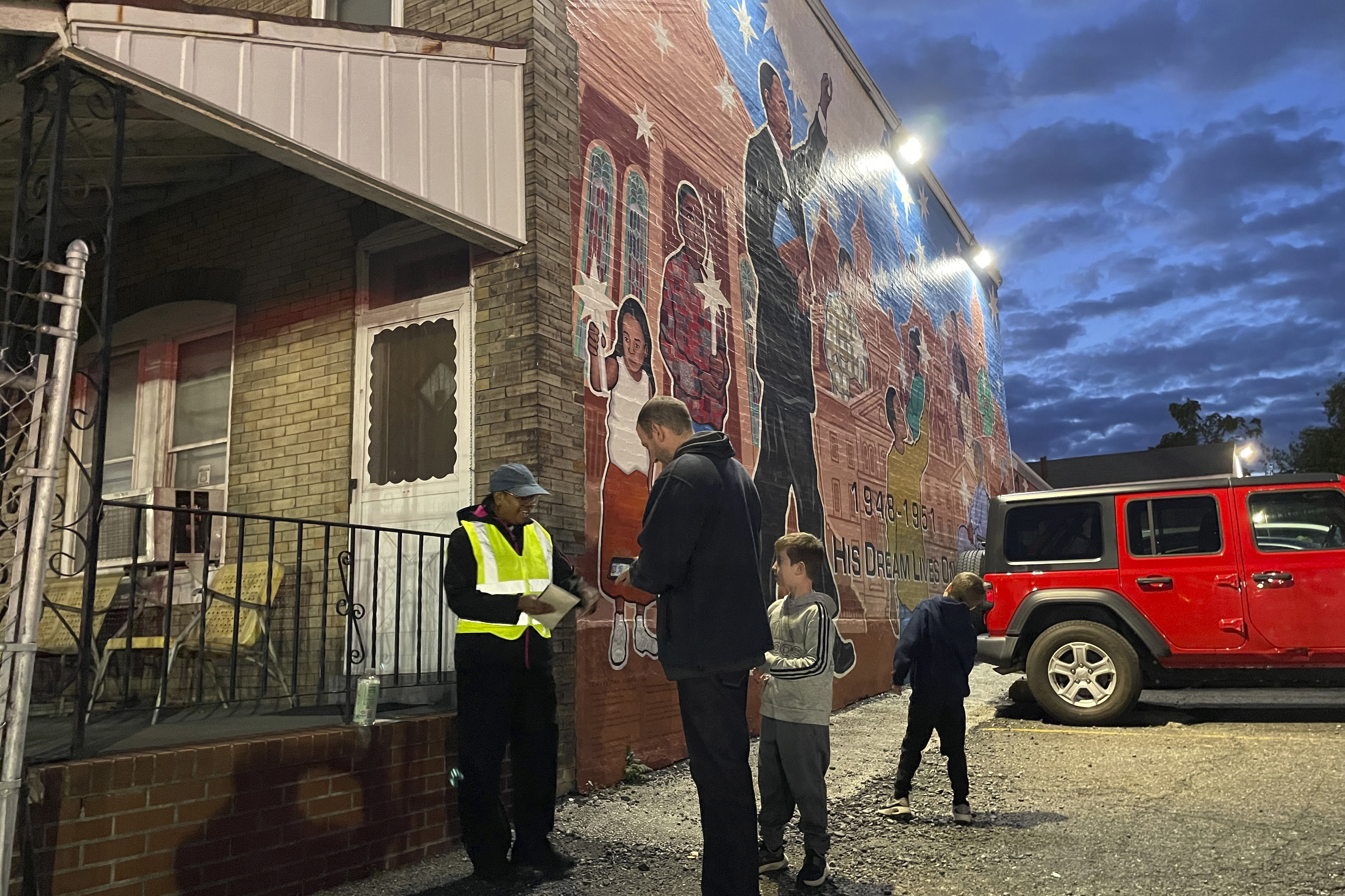 Philadelphia Union soccer fan Abe Gitterman, center, with his children, pays Calvary Baptist Church member Lisa Lewis, left, a fee for parking at the church lot in Chester, Pa., on Saturday, Oct. 7, 2023, in front of a mural that pays homage to Martin Luther King Jr., who attended the church as seminarian. The church, near Philadelphia Union's Subaru Park, has transformed its parking lot into game-day fundraisers for charities, ministries and a new speaker system that will allow Calvary to broadcast its services online.