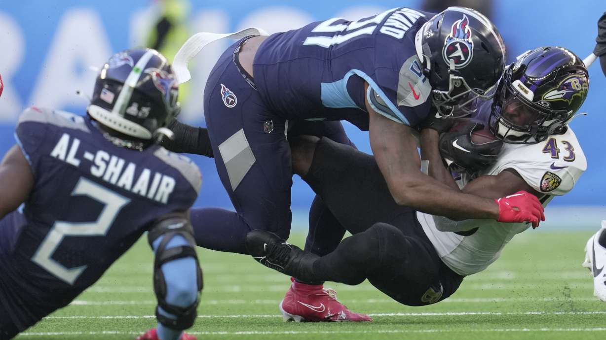 Tennessee Titans safety Kevin Byard, center, tackles Baltimore Ravens running back Justice Hill (43) during the first half of an NFL football game Sunday, Oct. 15, 2023, at the Tottenham Hotspur stadium in London.