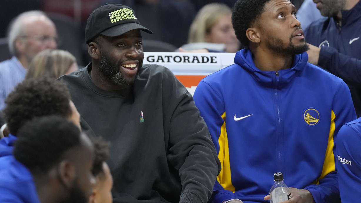 Injured Golden State Warriors forward Draymond Green, left, watches from the bench next to forward Rudy Gay during the first half of an NBA preseason basketball game against the San Antonio Spurs in San Francisco, Friday, Oct. 20, 2023.