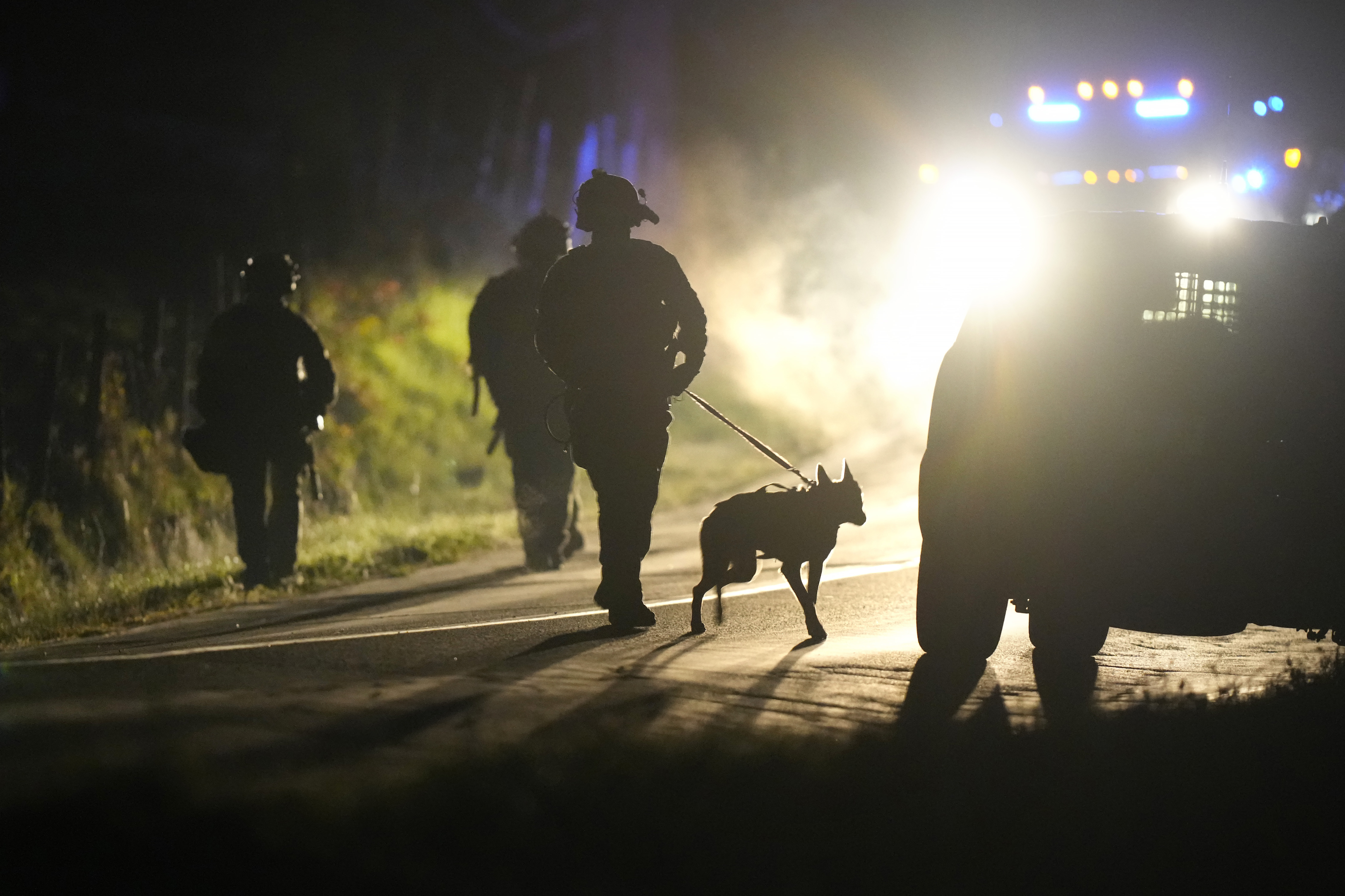 A member of law enforcement walks with a police dog outside a property on Meadow Road, in Bowdoin, Maine, Thursday.