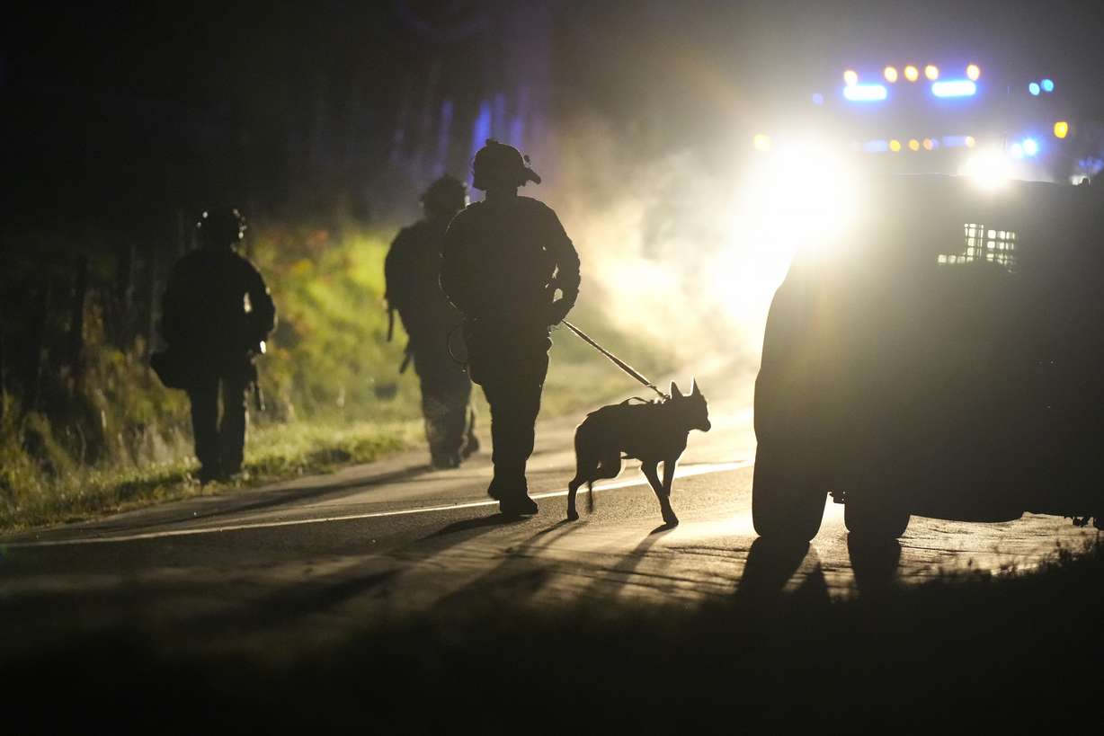 A member of law enforcement walks with a police dog outside a property on Meadow Road, in Bowdoin, Maine, Thursday.