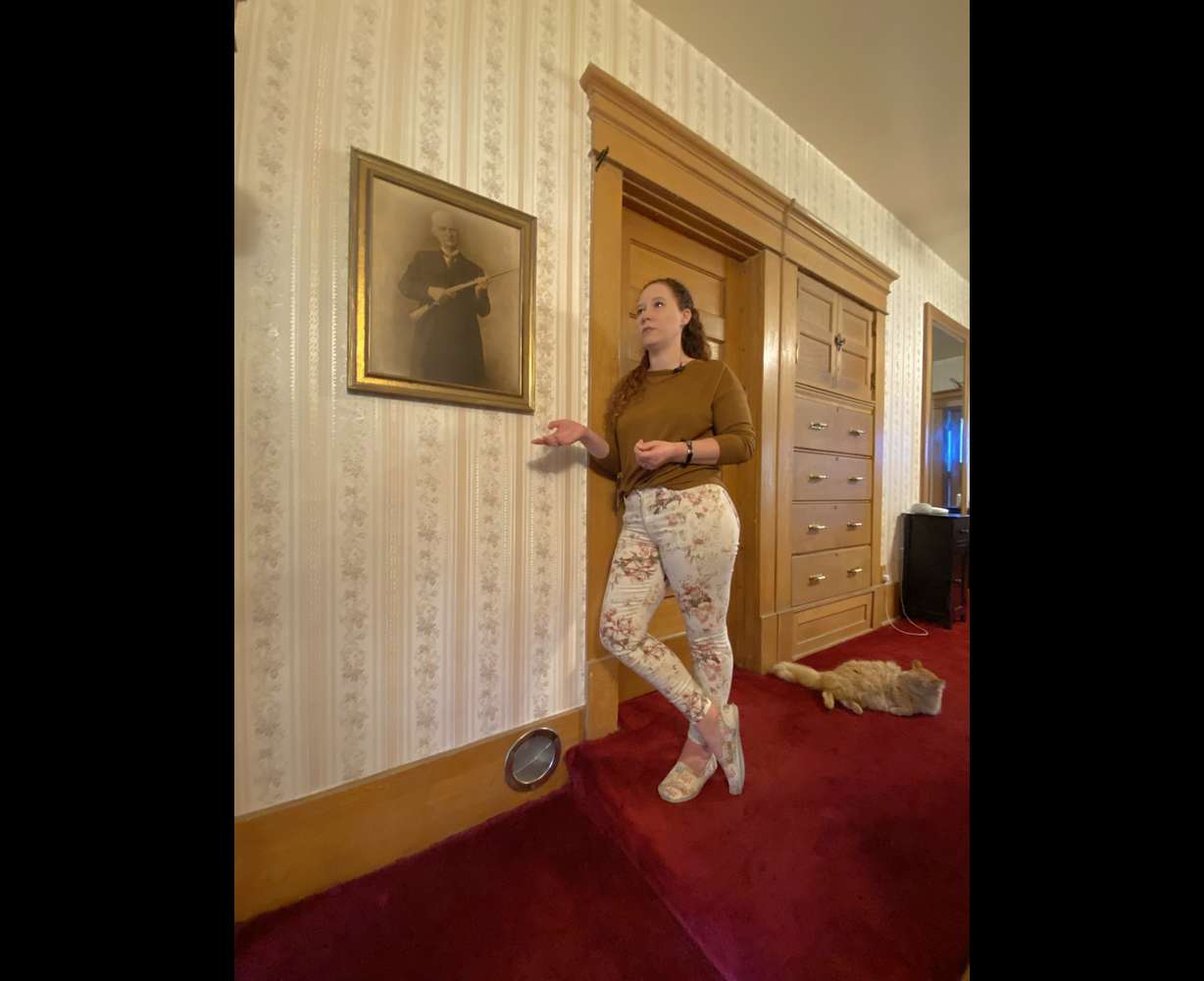Jackie Loveland stands next to a photo of John M. Browning. Loveland and her husband live in the historic Browning Mansion and feel it may be haunted.