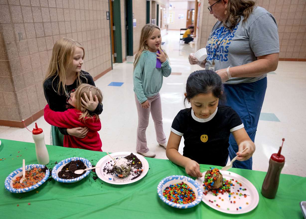 Sisters Jazzmyn and Jill Brems hug while making candy apples with students Leda Meek and Masina Irons and attendance secretary Heather Lane at Whittier Elementary School in West Valley on Friday. The students earned the opportunity to participate in the activity by improving her attendance.