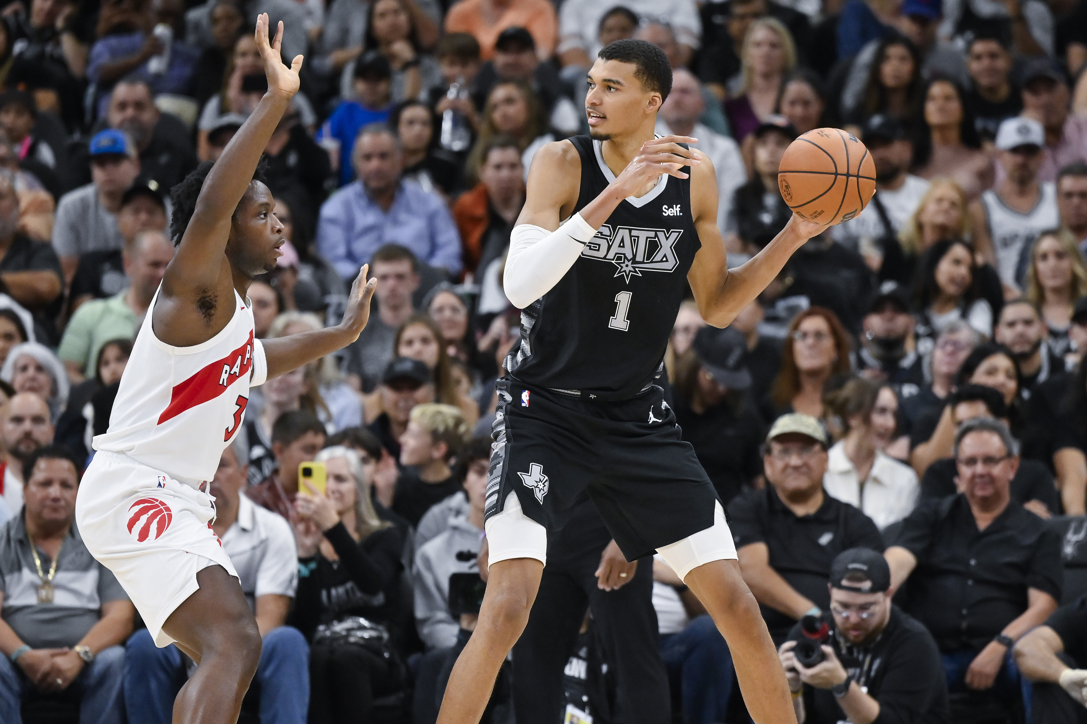 San Antonio Spurs' Victor Wembanyama (1) looks to pass the ball as he is defended by Toronto Raptors' O.G. Anunoby, left, during the second half of an NBA basketball game, Sunday, Nov. 5, 2023, in San Antonio.
