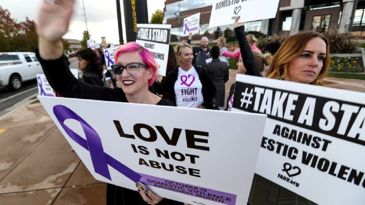 Domestic violence survivor Jenny Andrus, left, waves to motorists as she participates in a honk and wave during the West Valley City Victim Service’s Domestic Violence Awareness Night at the West Valley City Hall on Oct. 23, 2018. Victim resource providers say they need additional help meeting the surge in demand.