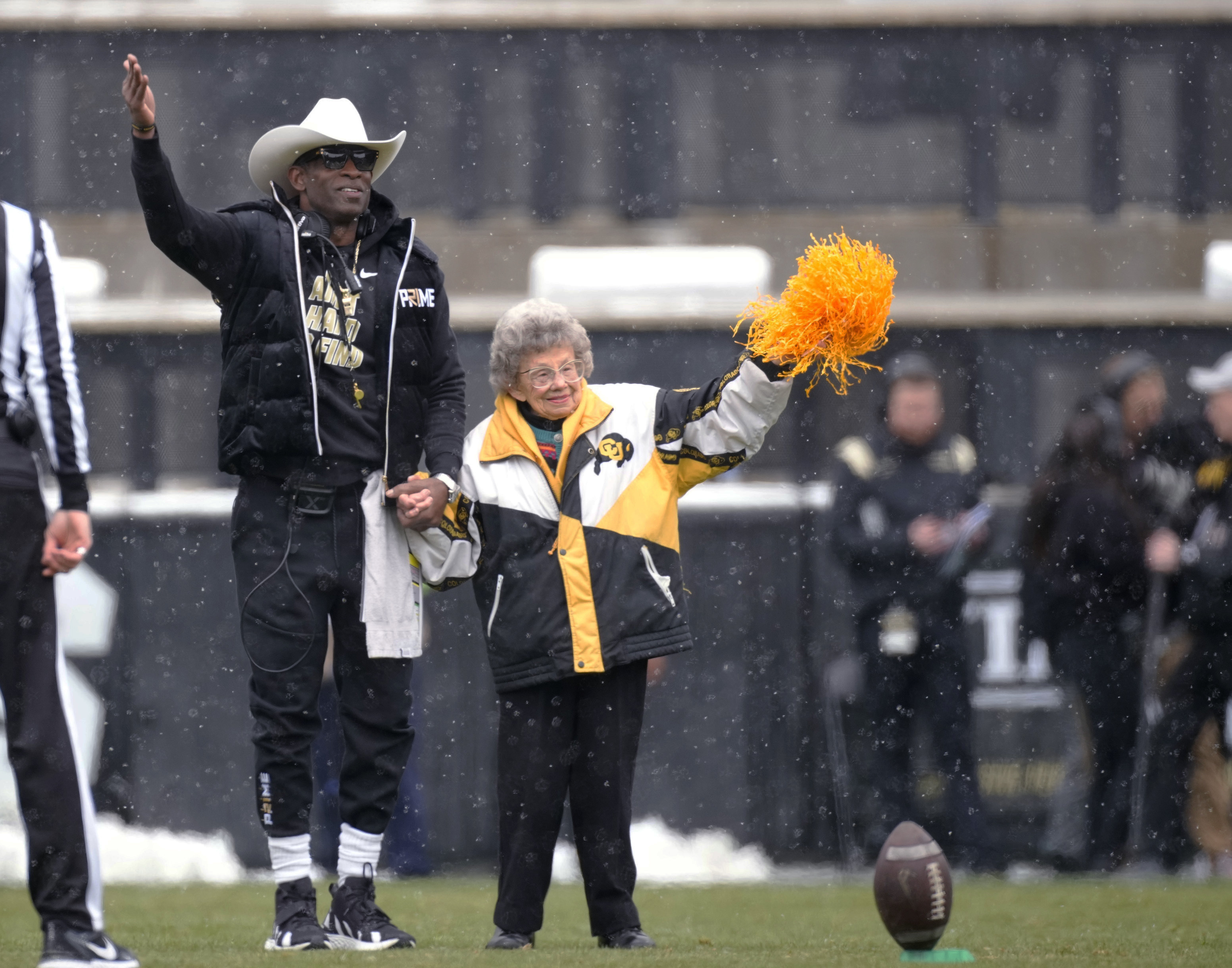 FILE - Colorado coach Deion Sanders, left, leads longtime supporter Peggy Coppom to kick the football before the team's spring practice NCAA college football game April 22, 2023, in Boulder, Colo. Coppom, who turns 99 on Sunday, is royalty. She’s a fixture at Buffaloes football and basketball games and couldn’t be more elated that after a 13-season move to the Pac-12, the school is making the switch back to the Big 12 next year. She does lament, though, that traditional conference rival Nebraska has moved on the Big Ten.