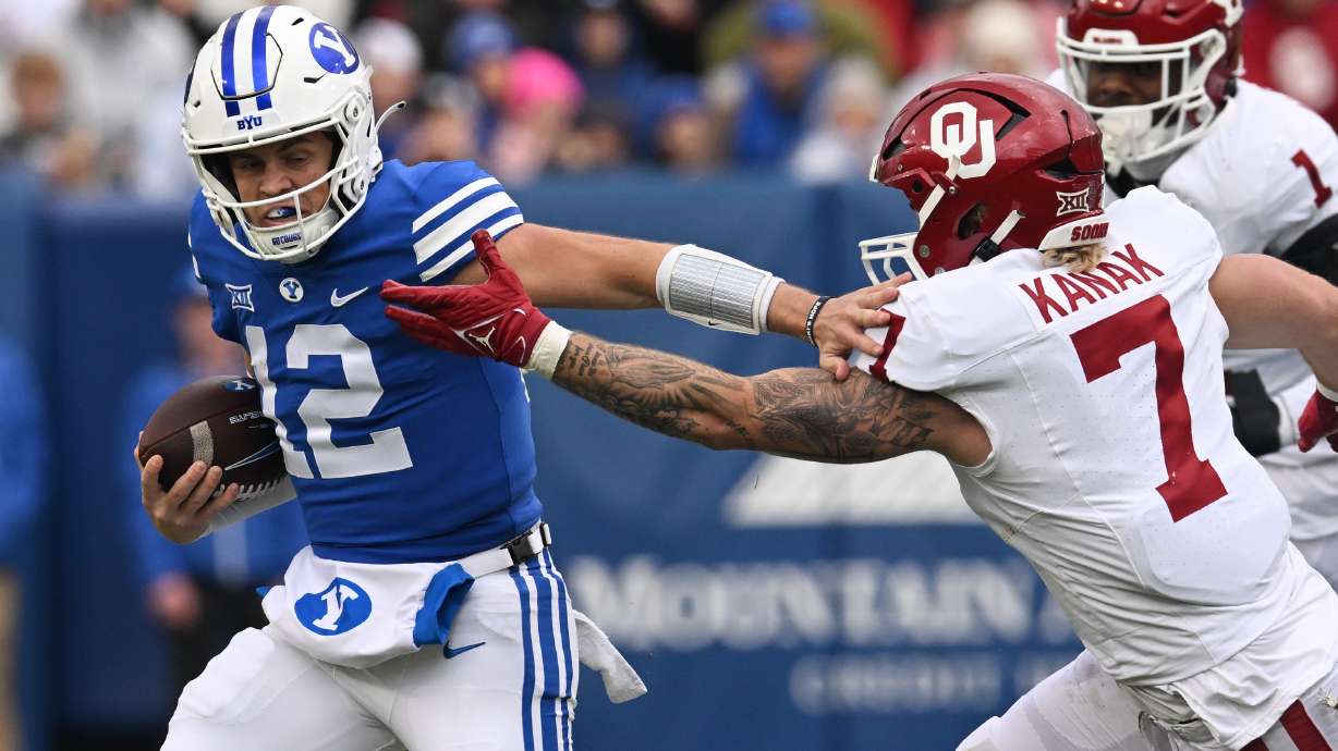 Young Cougars quarterback Jake Retzlaff (12) pushes Oklahoma linebacker Jaren Kanak (7) away during a run as BYU and Oklahoma play at LaVell Edwards Stadium in Provo on Saturday, Nov. 18, 2023.