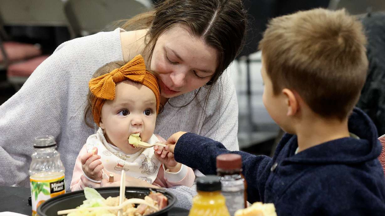 Jesse James helps feed his sister Amara Mayer as their mother Maia Mayer watches at the Larry H. Miller Company and Larry H. and Gail Miller Family Foundation’s annual Season of Thanksgiving Dinner and Service Event Salt Lake City on Monday.