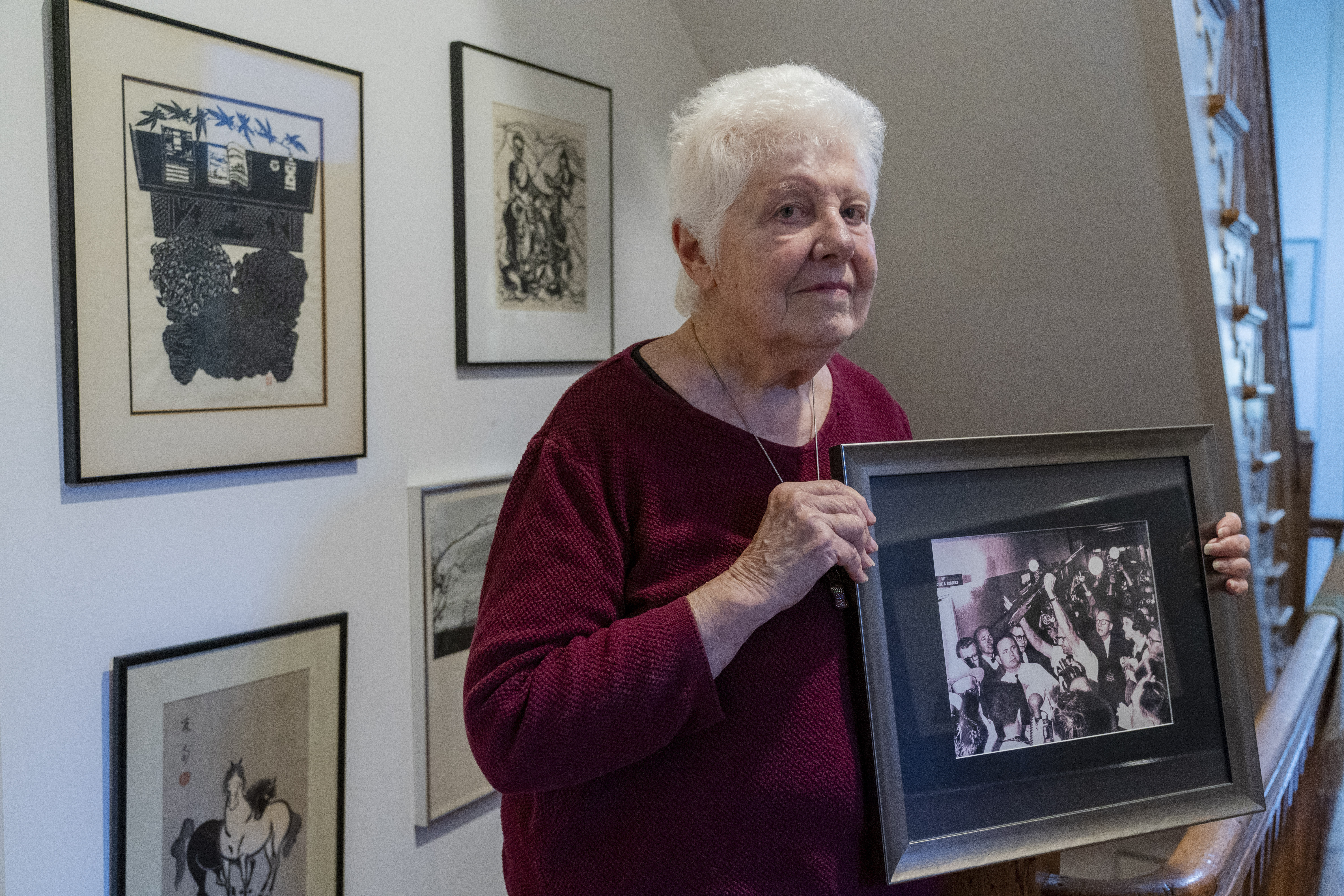Peggy Simpson holds a photograph of law enforcement carrying Lee Harvey Oswald's gun through a hallway packed with reporters, Friday, at her home in Washington. Simpson, a former Associated Press reporter, is among the last surviving witnesses to the events surrounding the assassination of Kennedy are among those sharing their stories as the nation marks the 60th anniversary.