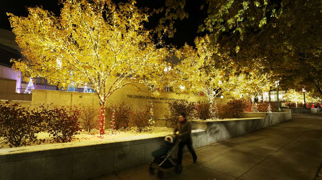 A woman pushes a stroller on the sidewalk near the Christmas lights at The Church of Jesus Christ of Latter-day Saints' Conference Center in Salt Lake City on Nov. 29, 2022. The lights on Temple Square will be flipped on Friday, but ongoing construction will change where people can view them again this year.