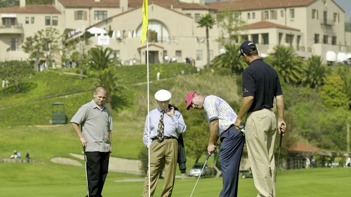 FILE - With the historic clubhouse in the background, Duffy Waldorf takes a practice putt at the 10th green as veteran teaching pro Eddie Merrins, in the tie, and golfer Arron Oberholser, right, watch during a practice session for the Nissan Open at Riviera Country Club, Feb. 18, 2003, in Los Angeles. Merrins died Wednesday, Nov. 22, 2023, at age 91.