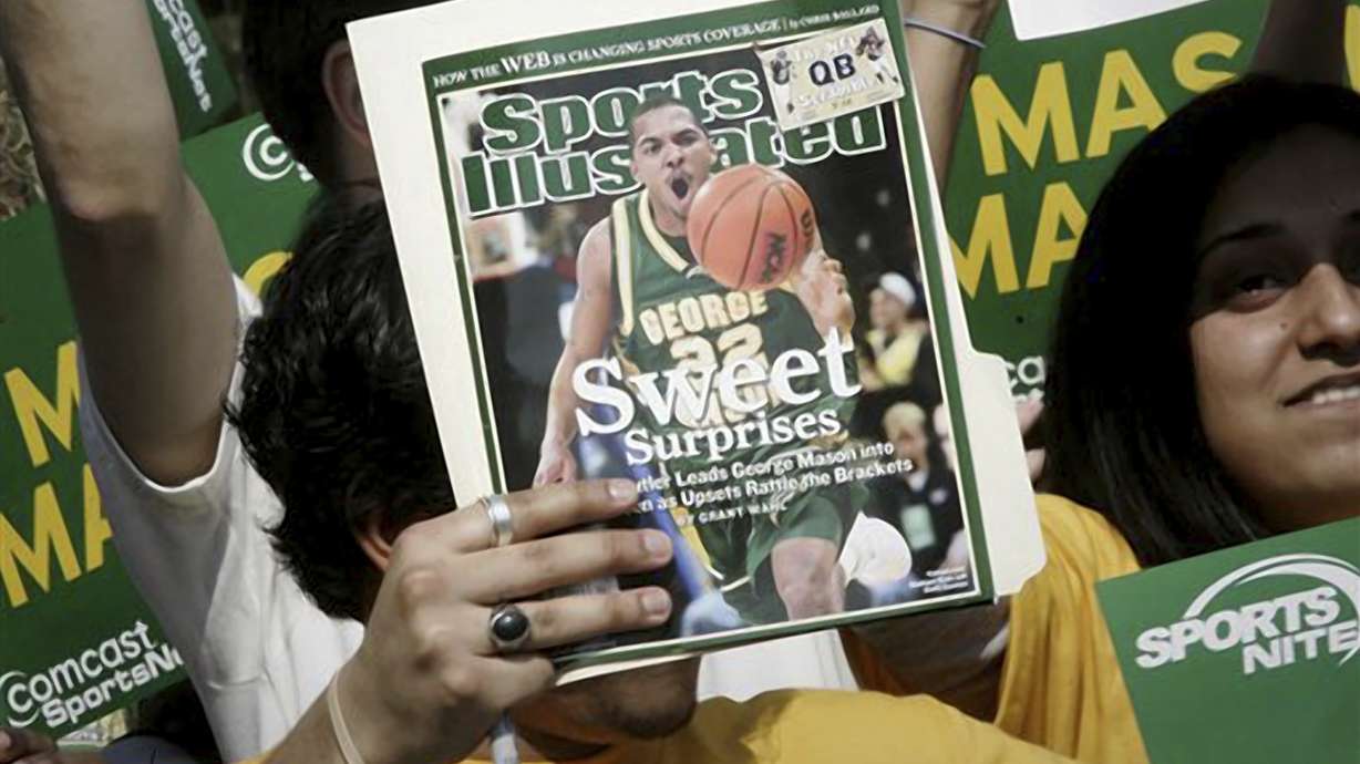 FILE - A George Mason University fan holds up a Sports Illustrated magazine at a send off for the team, March 29, 2006, in Fairfax, Va. Sports Illustrated is the latest media company damaged by being less than forthcoming about who or what is writing its stories. The website Futurism reported that the once-grand magazine used articles with “authors” who apparently don't exist, with photos generated by AI. The magazine denied claims that some articles themselves were AI-assisted, but has cut ties with a vendor it hired to produce the articles.