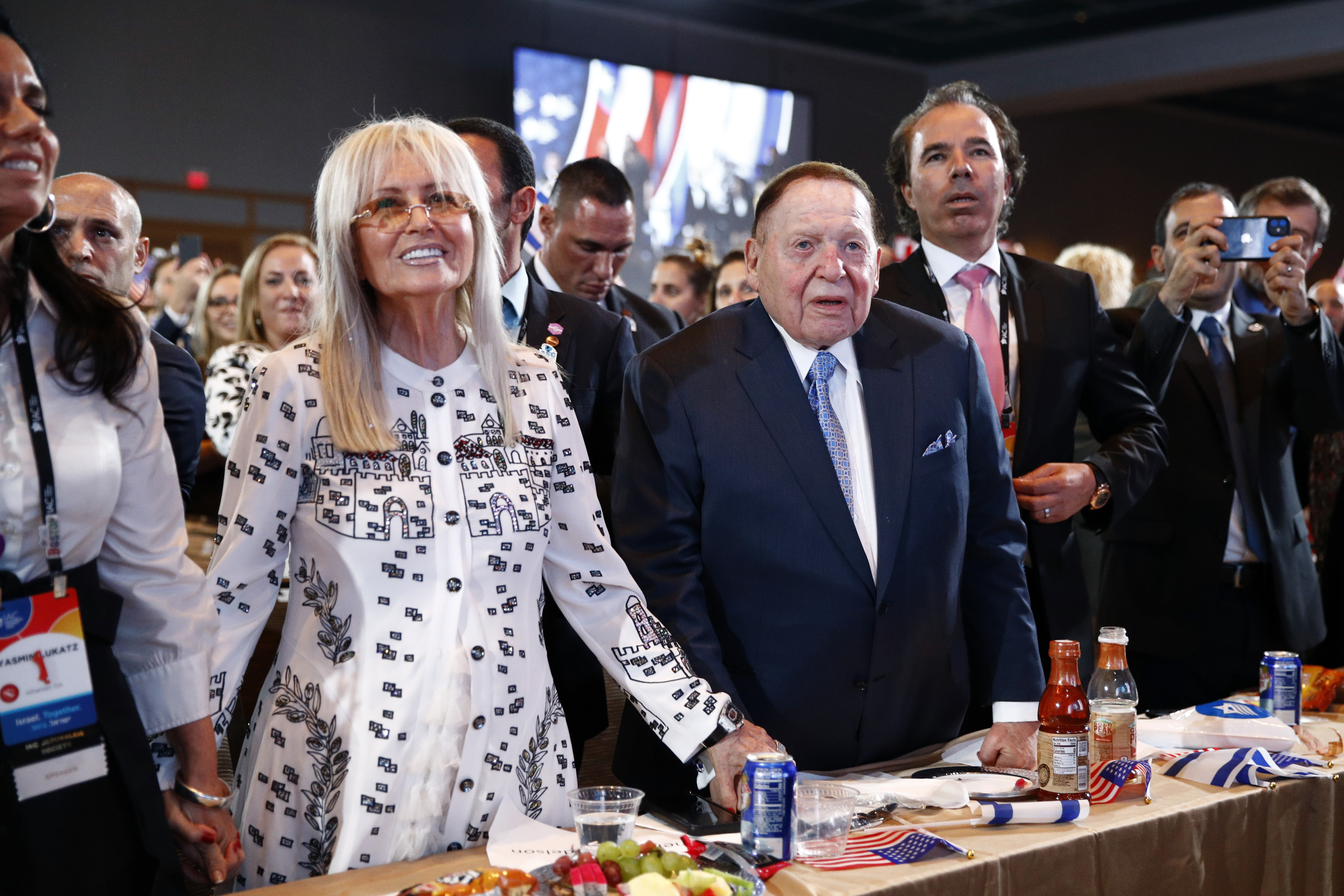 FILE - Las Vegas Sands Corporation Chief Executive and Republican mega donor Sheldon Adelson, center, and his wife, Miriam Adelson, left, listen as President Donald Trump speaks at the Israeli American Council National Summit in Hollywood, Fla., Saturday, Dec. 7, 2019. Miriam Adelson, the controlling shareholder of casino company Las Vegas Sands Corp., plans to sell $2 billion in company stock and buy an unspecified professional sports franchise, the company announced Tuesday, Nov. 28, 2023. Dallas Mavericks owner Mark Cuban is working on a deal to sell a majority stake in the NBA franchise to the Adelson family, a person with knowledge of the talks said late Tuesday.