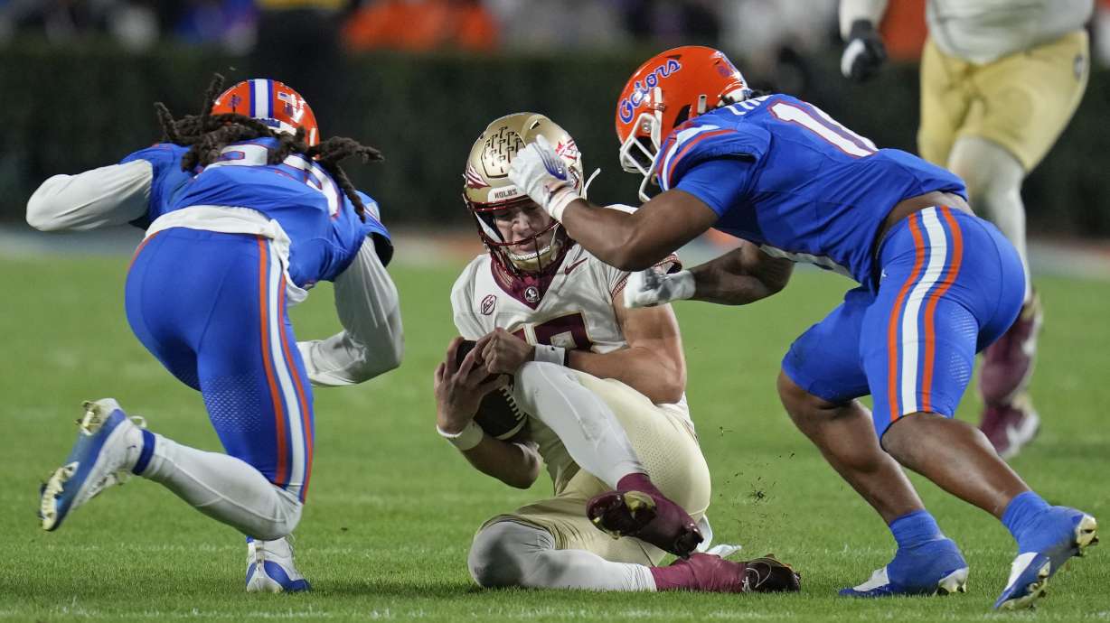 Florida cornerback Jaydon Hill, left, and safety Bryce Thornton, right, hit Florida State quarterback Tate Rodemaker, center, as he slides during the second half of an NCAA college football game, Saturday, Nov. 25, 2023, in Gainesville, Fla. Hill was charged with targeting and was ejected.