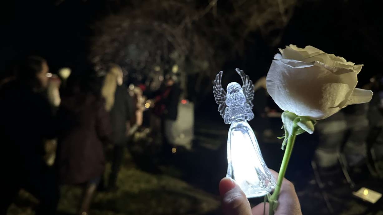 An attendee holds a rose and an angel light as people place flowers on the Angel of Hope statue at the annual Christmas Box Angel vigil in the Salt Lake City Cemetery on Wednesday. The event honors children who have died.
