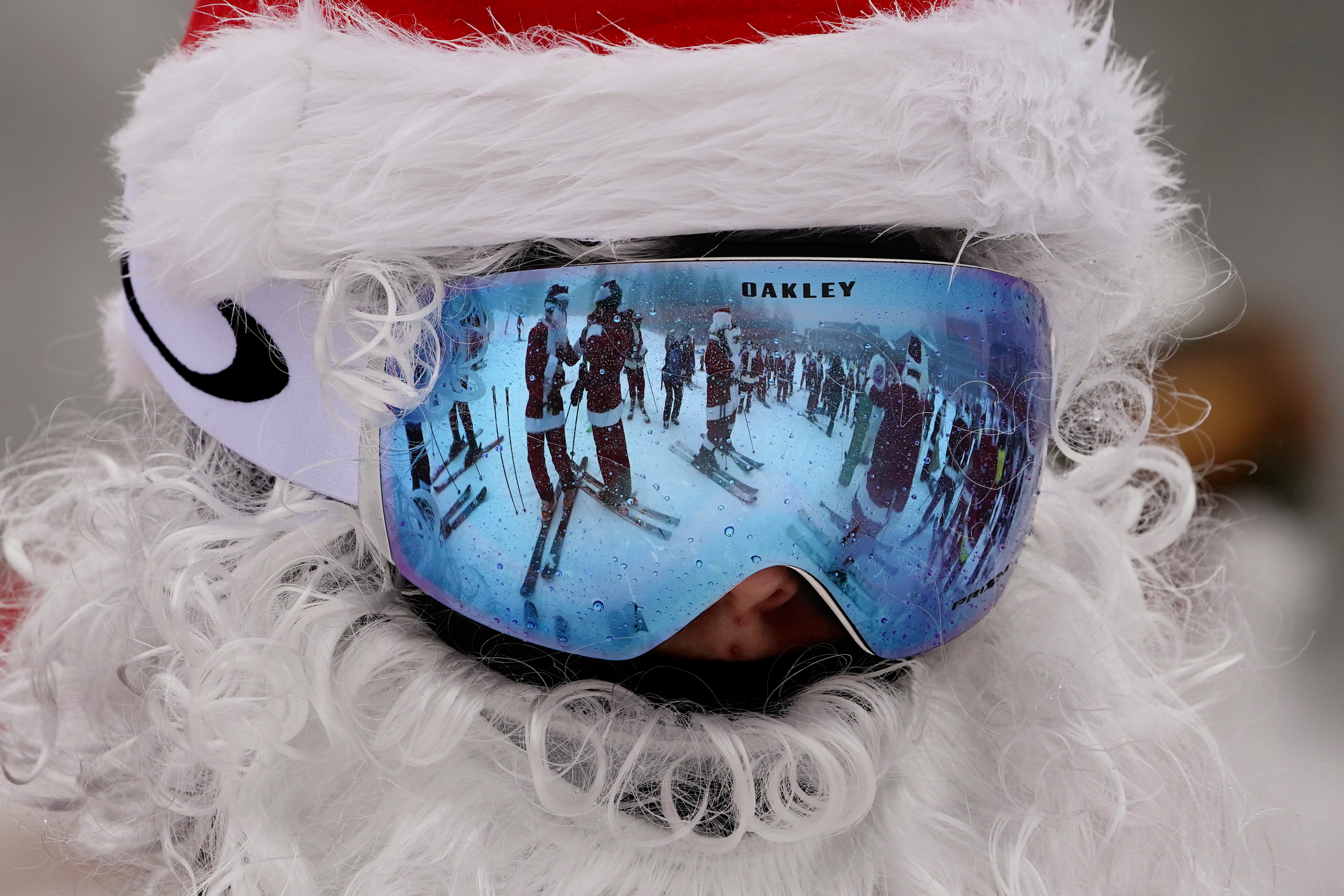 Skiers dressed as Santa Claus are reflected in another skier's goggles, Sunday, Dec. 10, 2023, at the Sunday River ski resort in Newry, Maine. The annual Santa Sunday event raises money for local charities.