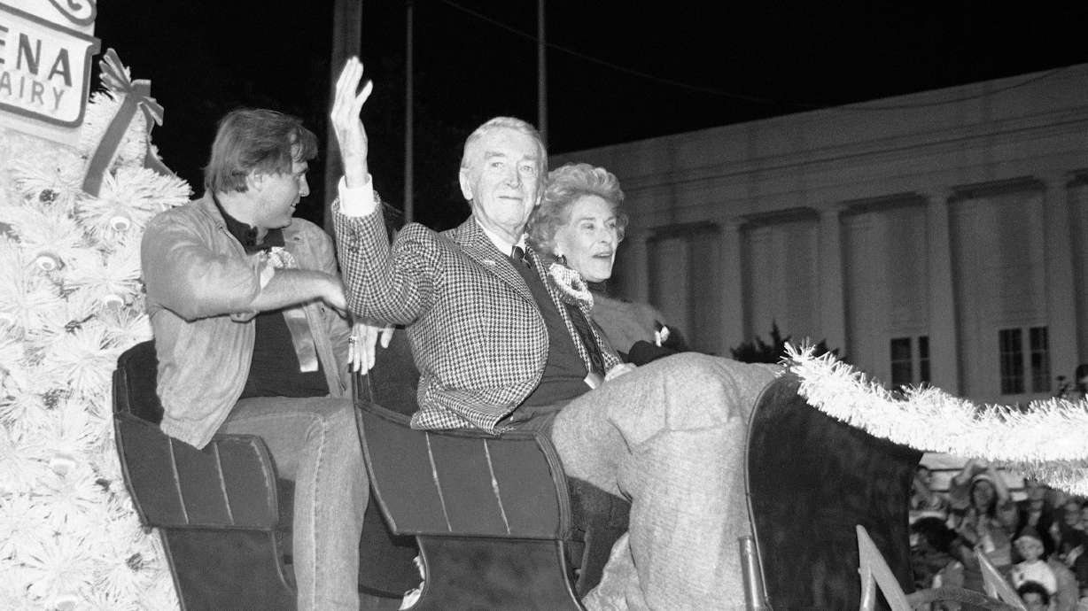 Actor Jimmy Stewart waves as he rides down Sunset Boulevard in the annual Christmas parade in Hollywood, Los Angeles on Nov. 30, 1986. At right is Stewart’s wife, Gloria, and left is actor Gil Gerald.